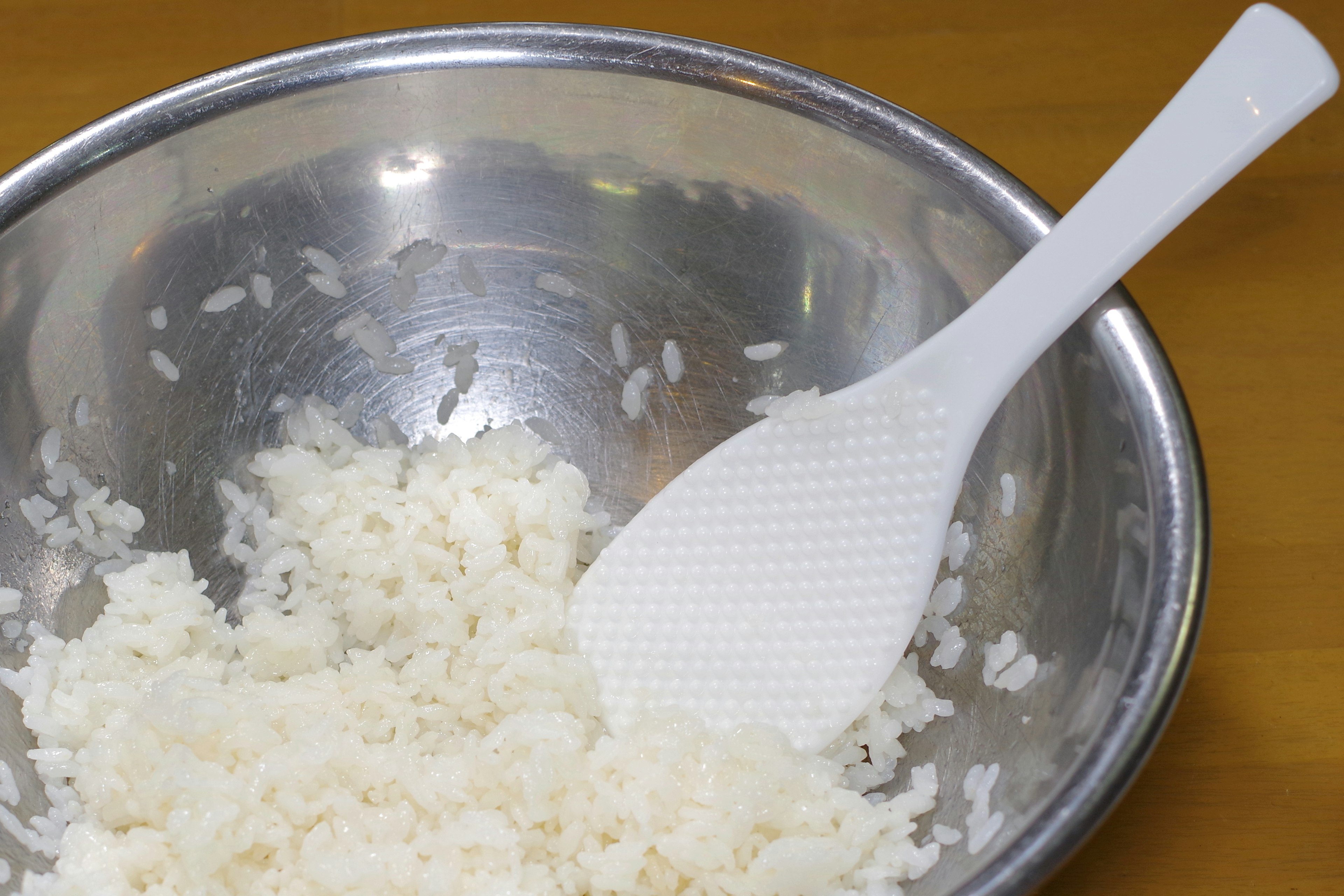 Fluffy rice in a silver bowl with a white spatula