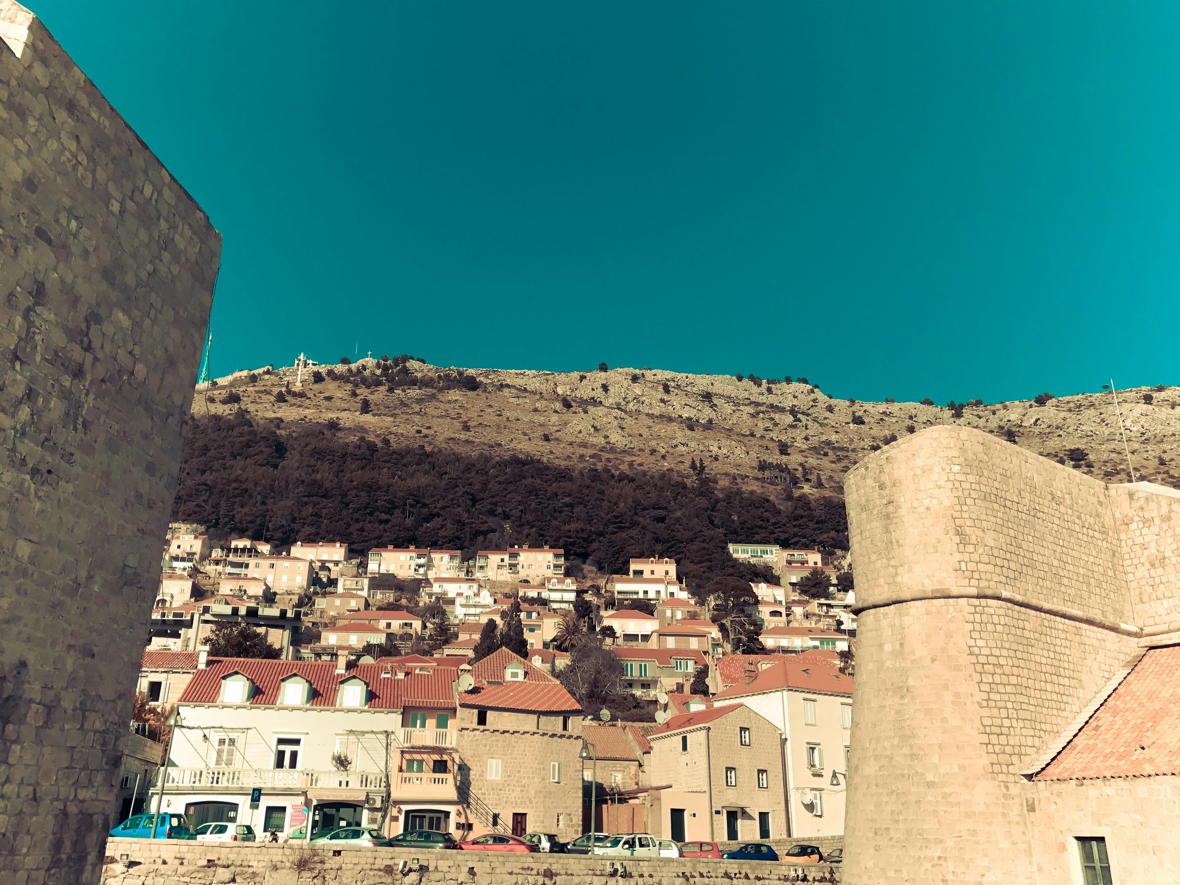 Houses on a hillside under a blue sky with stone walls in the foreground