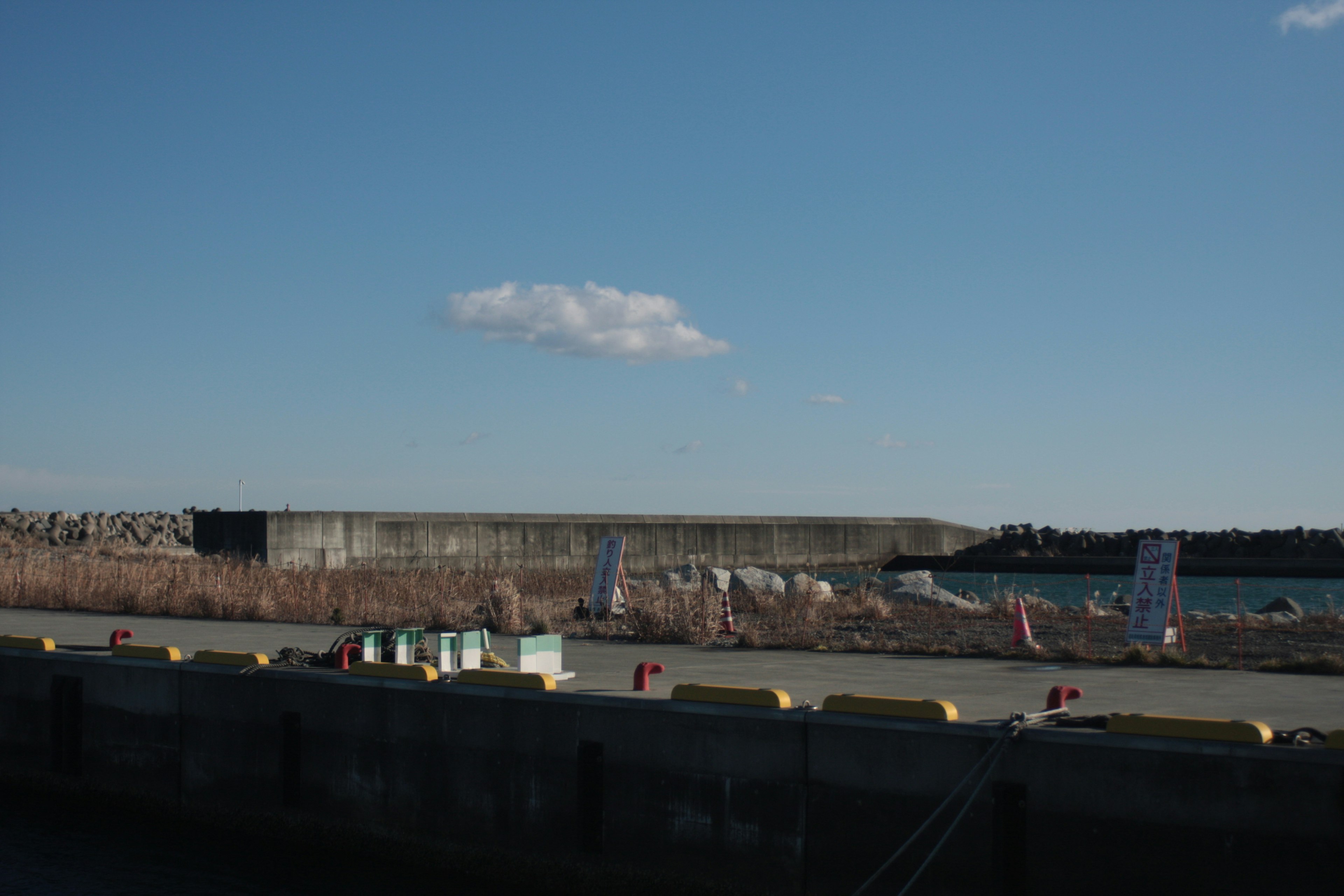 Hafenansicht unter blauem Himmel mit entferntem Wellenbrecher