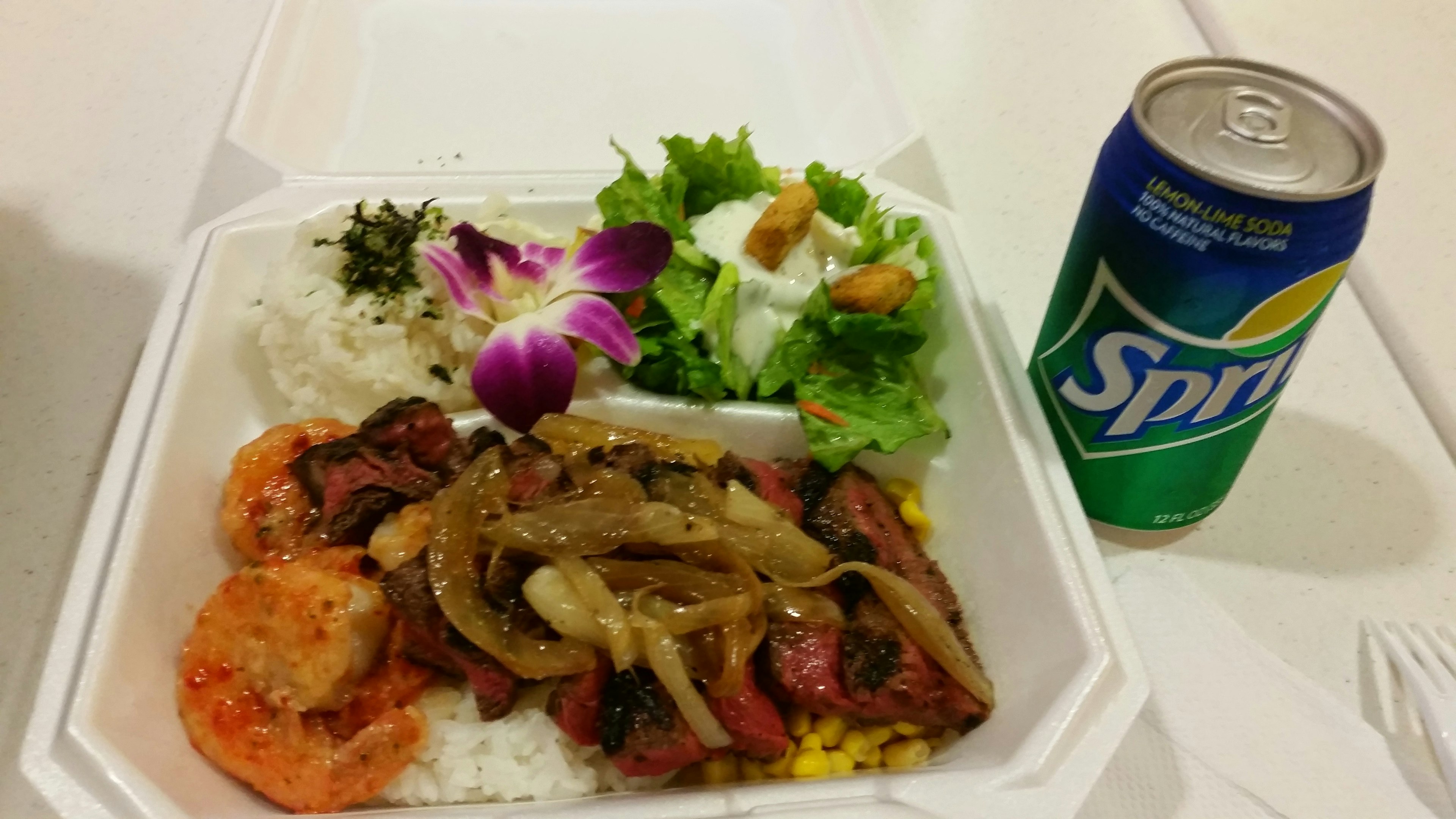 A meal served in a white container featuring shrimp, meat, onions, salad, and a can of Sprite