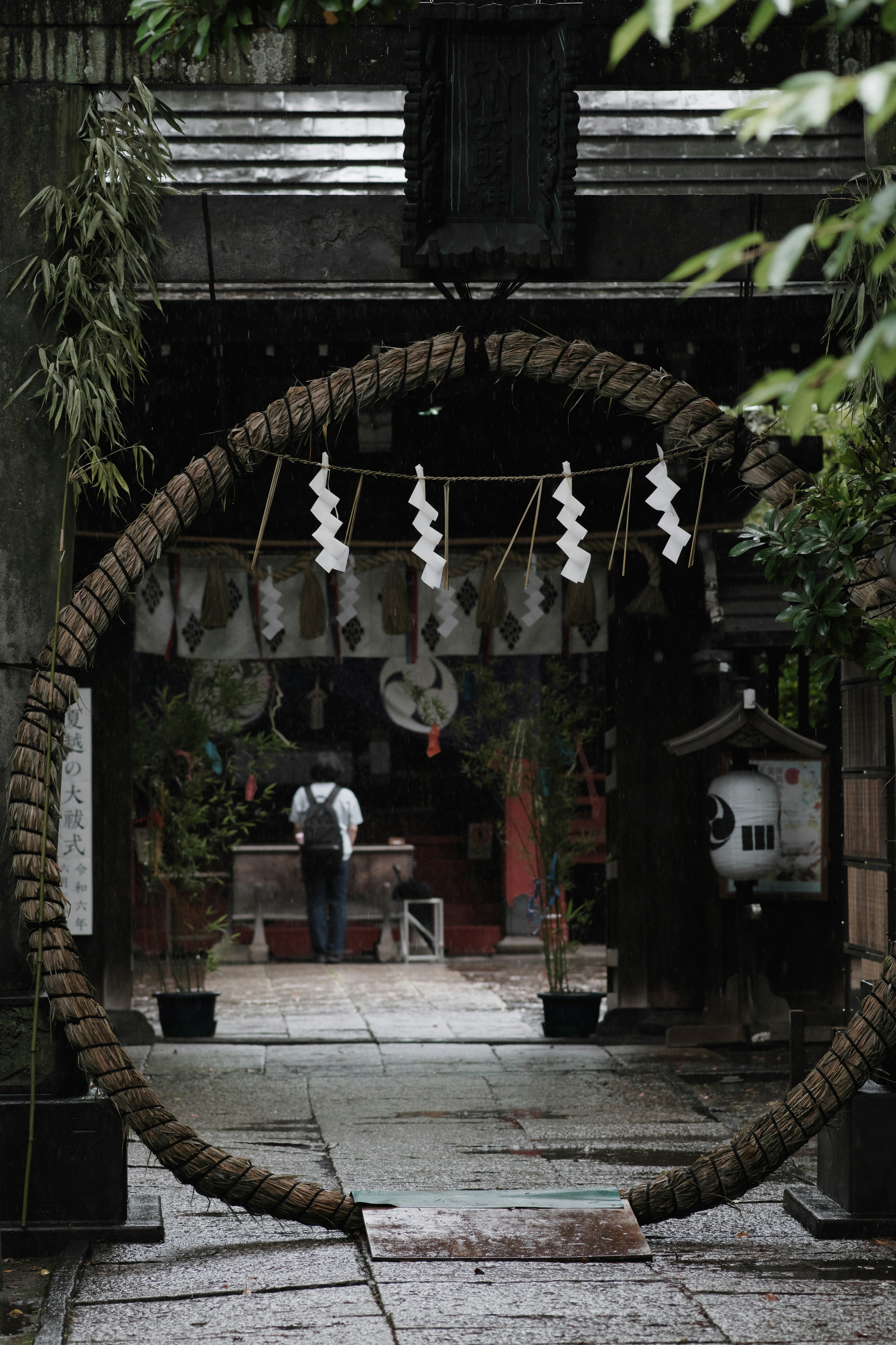 雨の日の神社の入り口を飾る大きな輪と白い飾りが印象的な風景