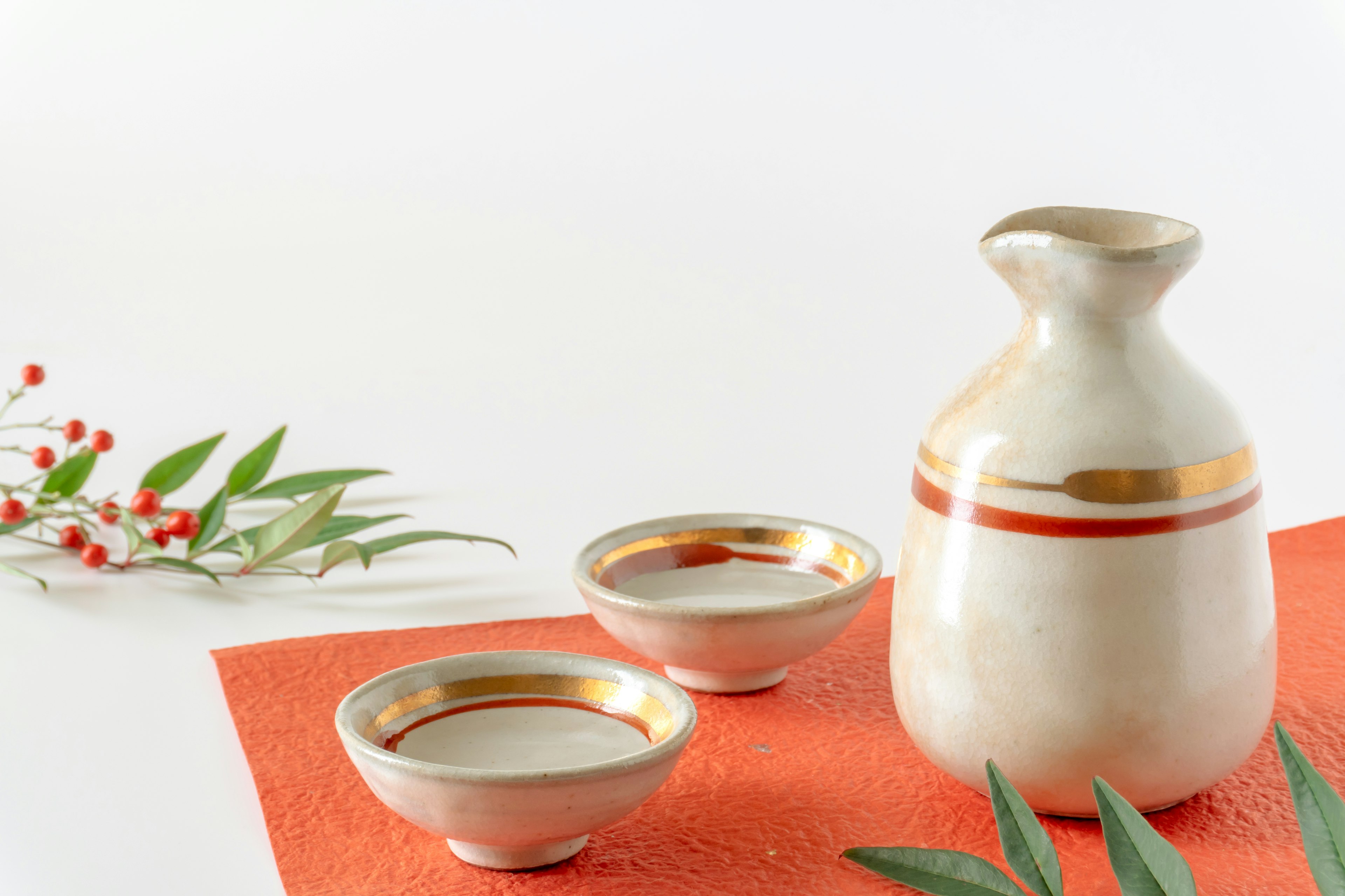 Set da sake in ceramica con una bottiglia e due coppe su sfondo bianco con strisce dorate