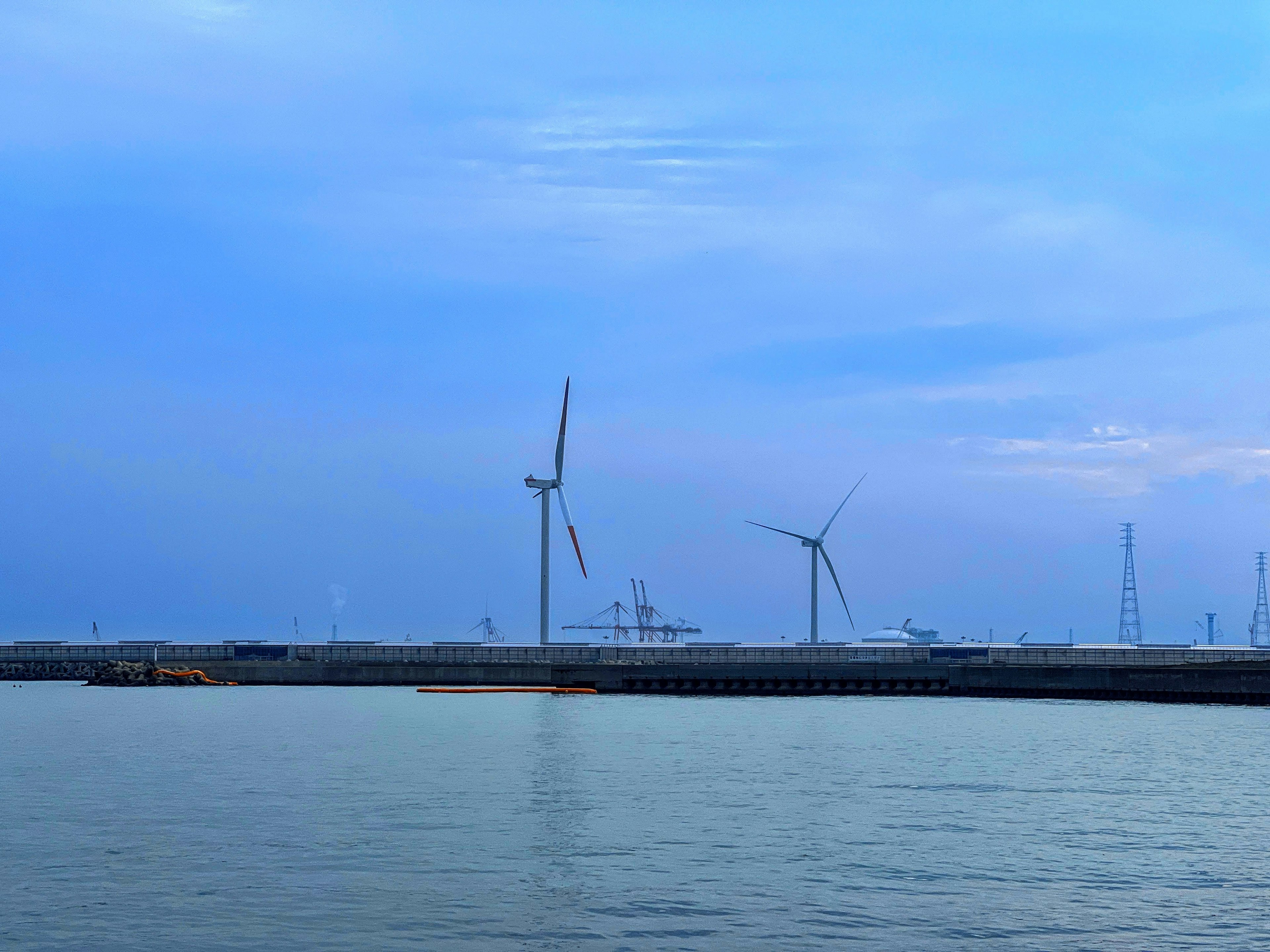 Küstenansicht mit Windkraftanlagen blauem Himmel und ruhigem Wasser