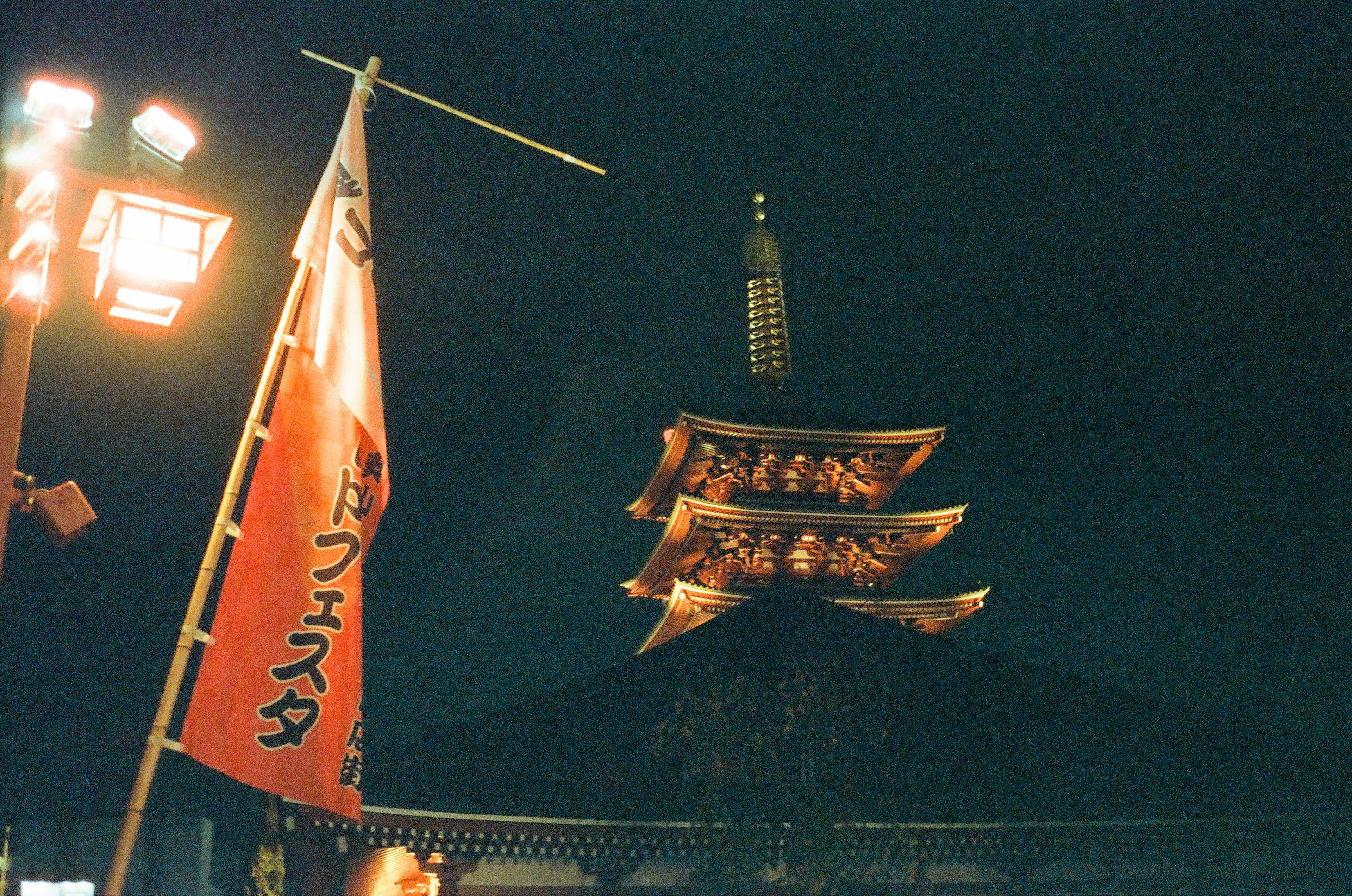 Illuminated pagoda at night with a red flag