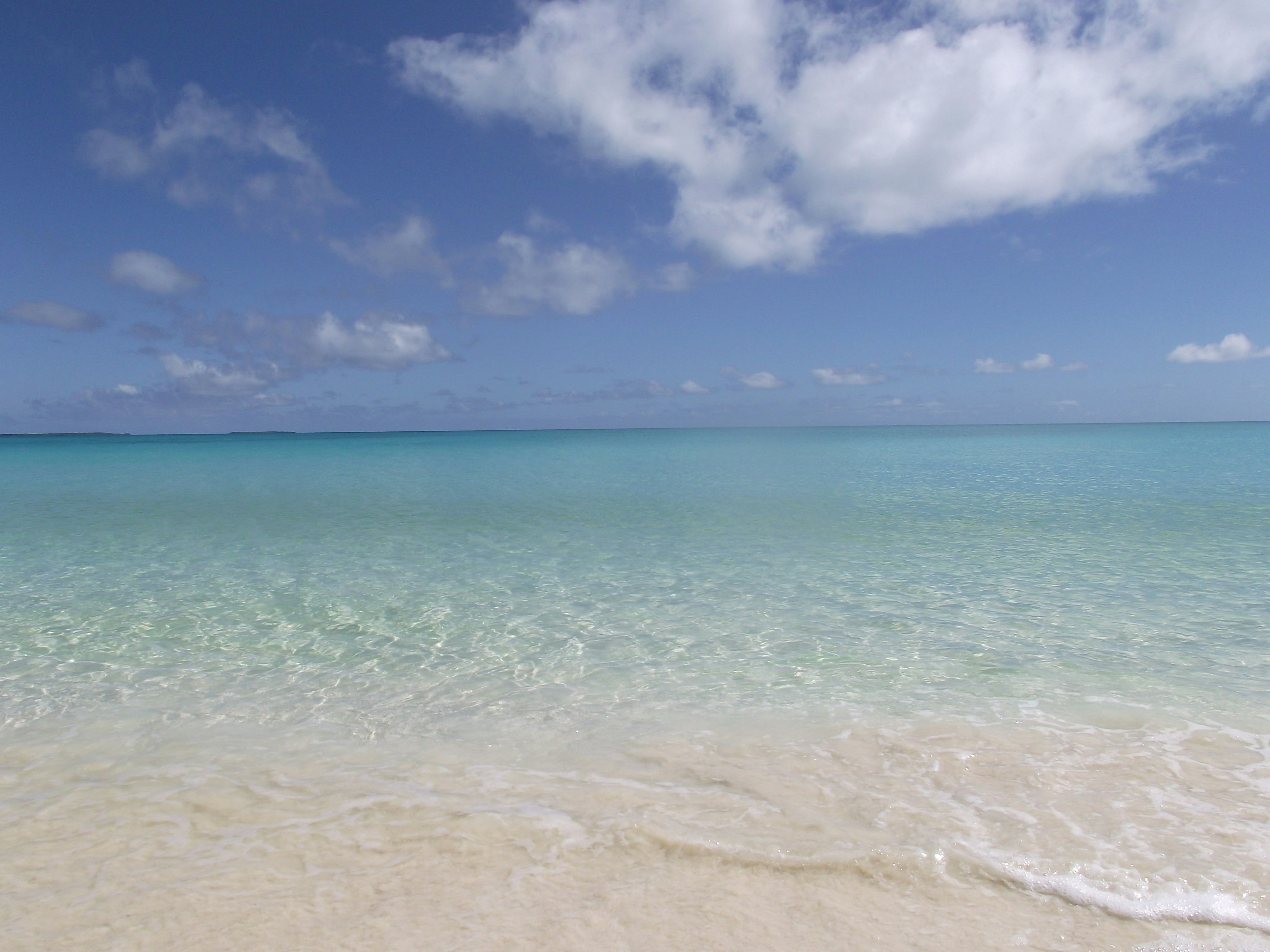 Klares türkisfarbenes Wasser trifft auf einen Sandstrand unter einem blauen Himmel