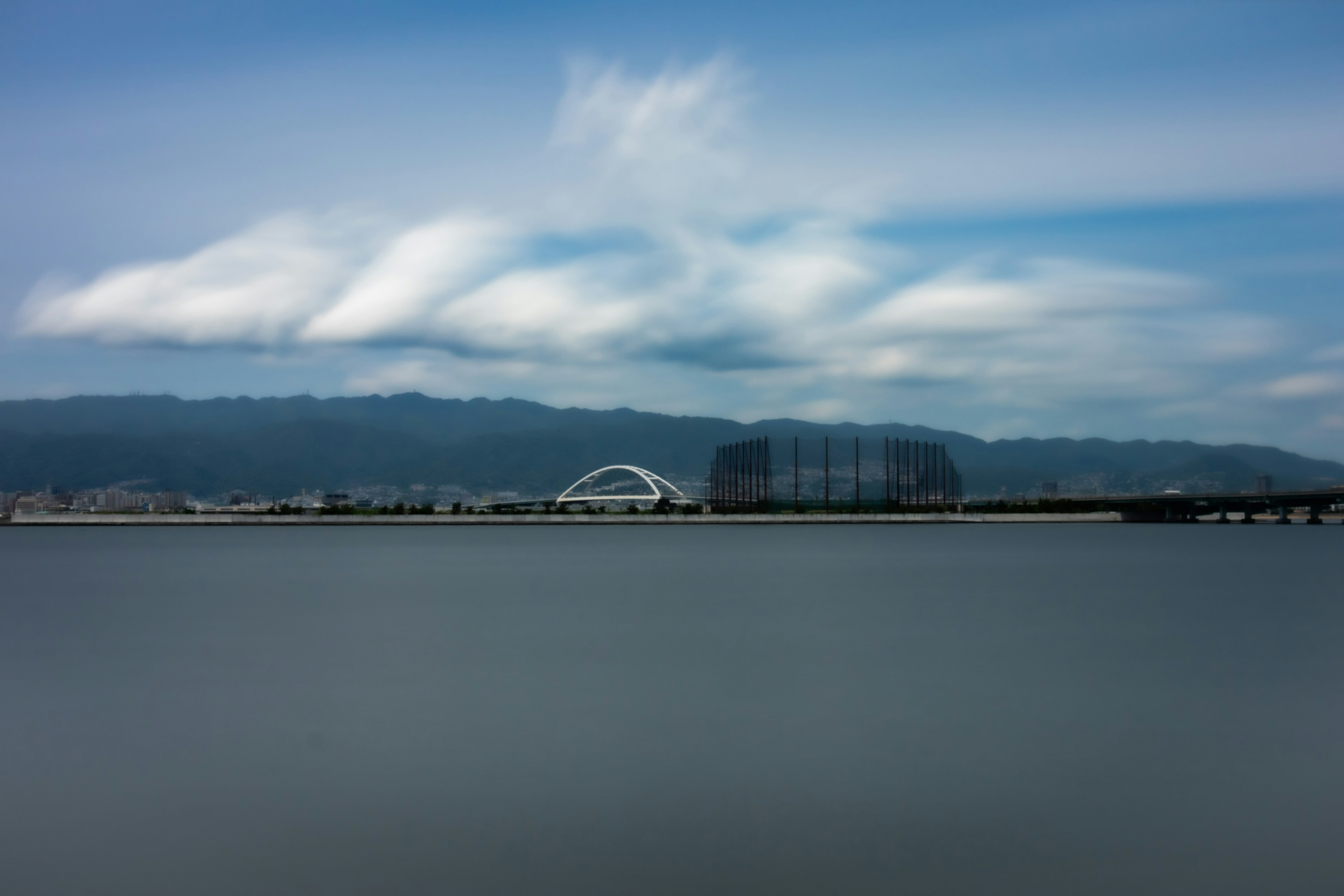 Serene water surface under a blue sky with clouds and mountains in the background