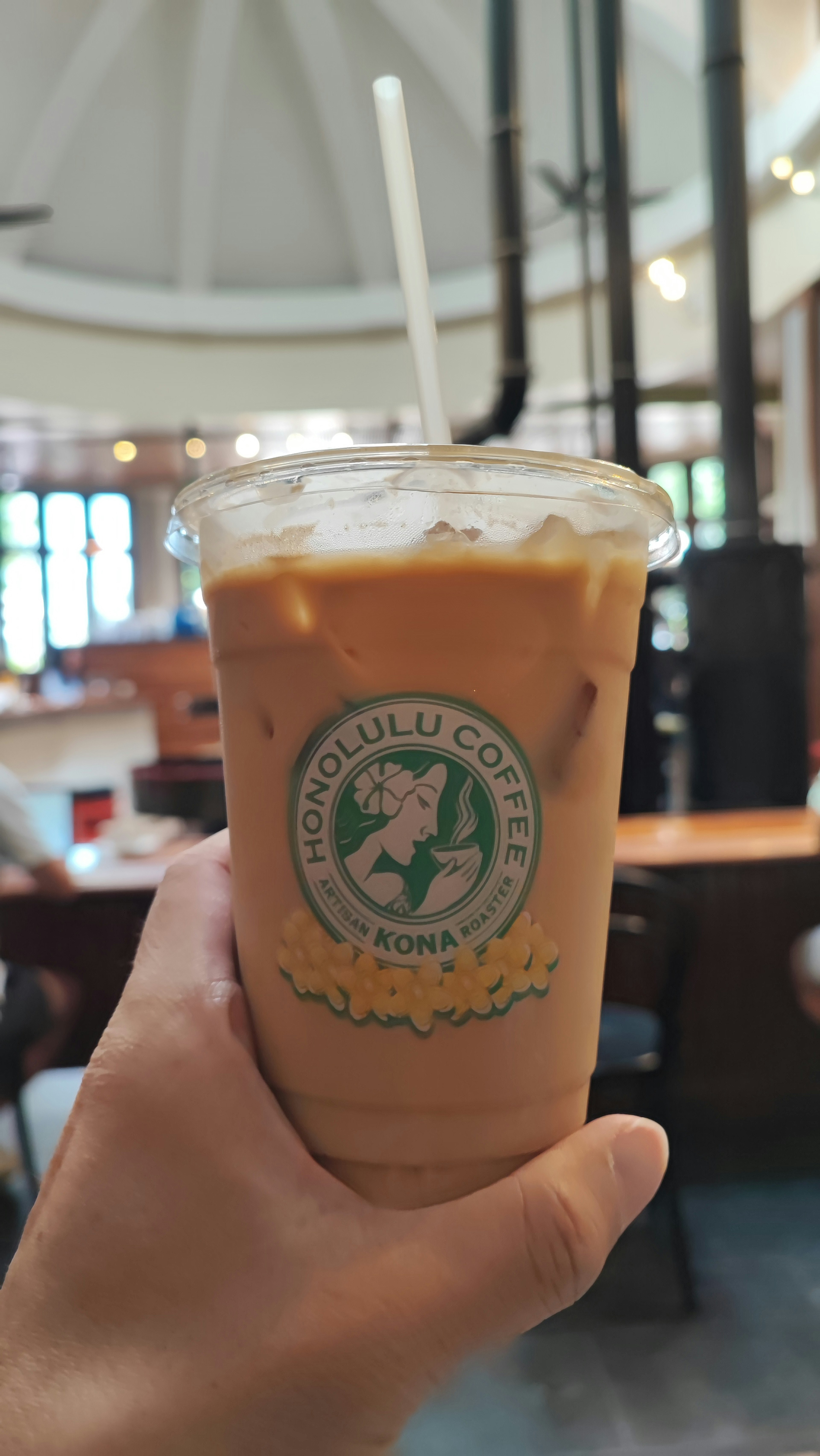 A hand holding an iced coffee in a café interior