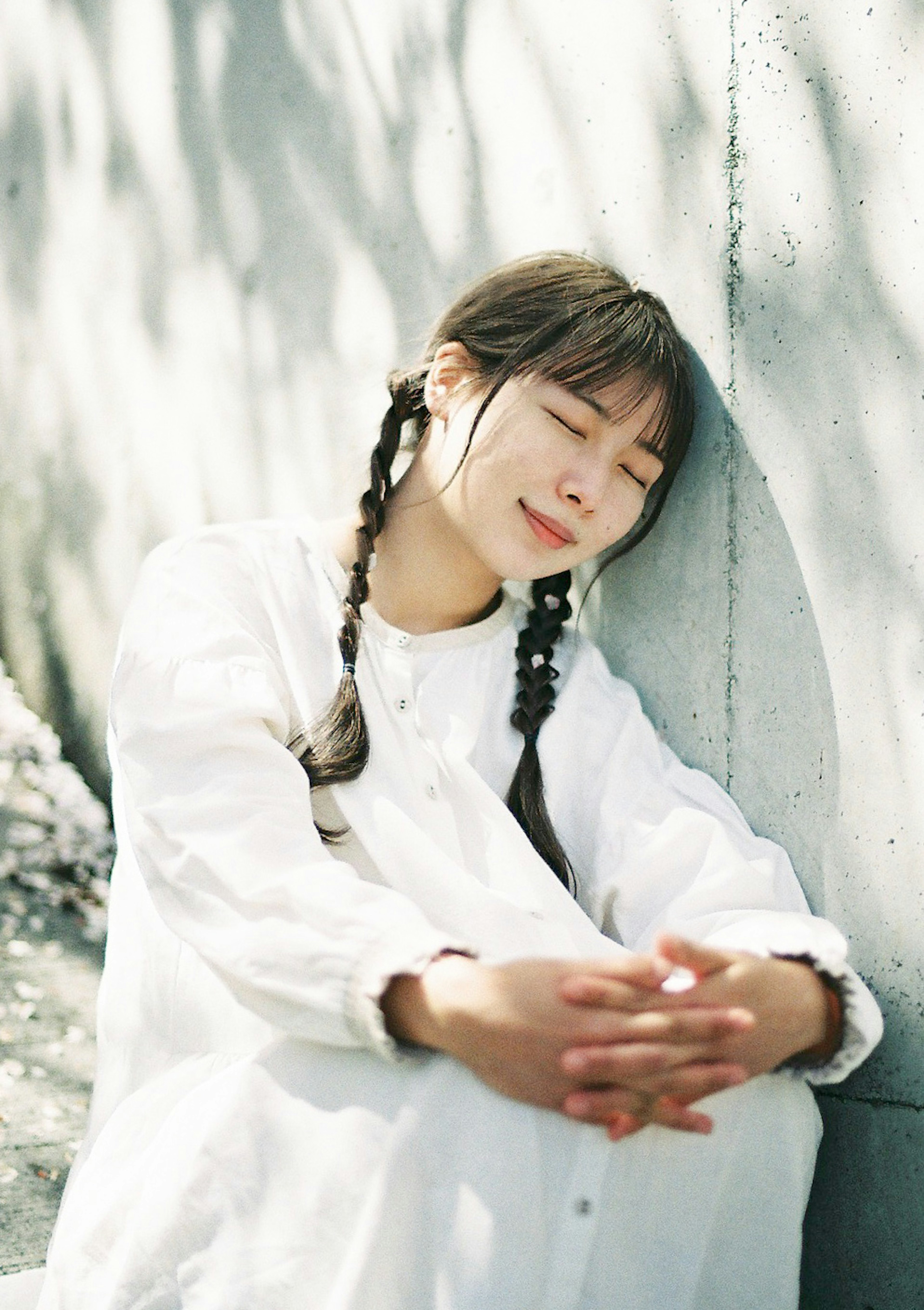 A woman in a white dress leaning against a wall with a gentle smile