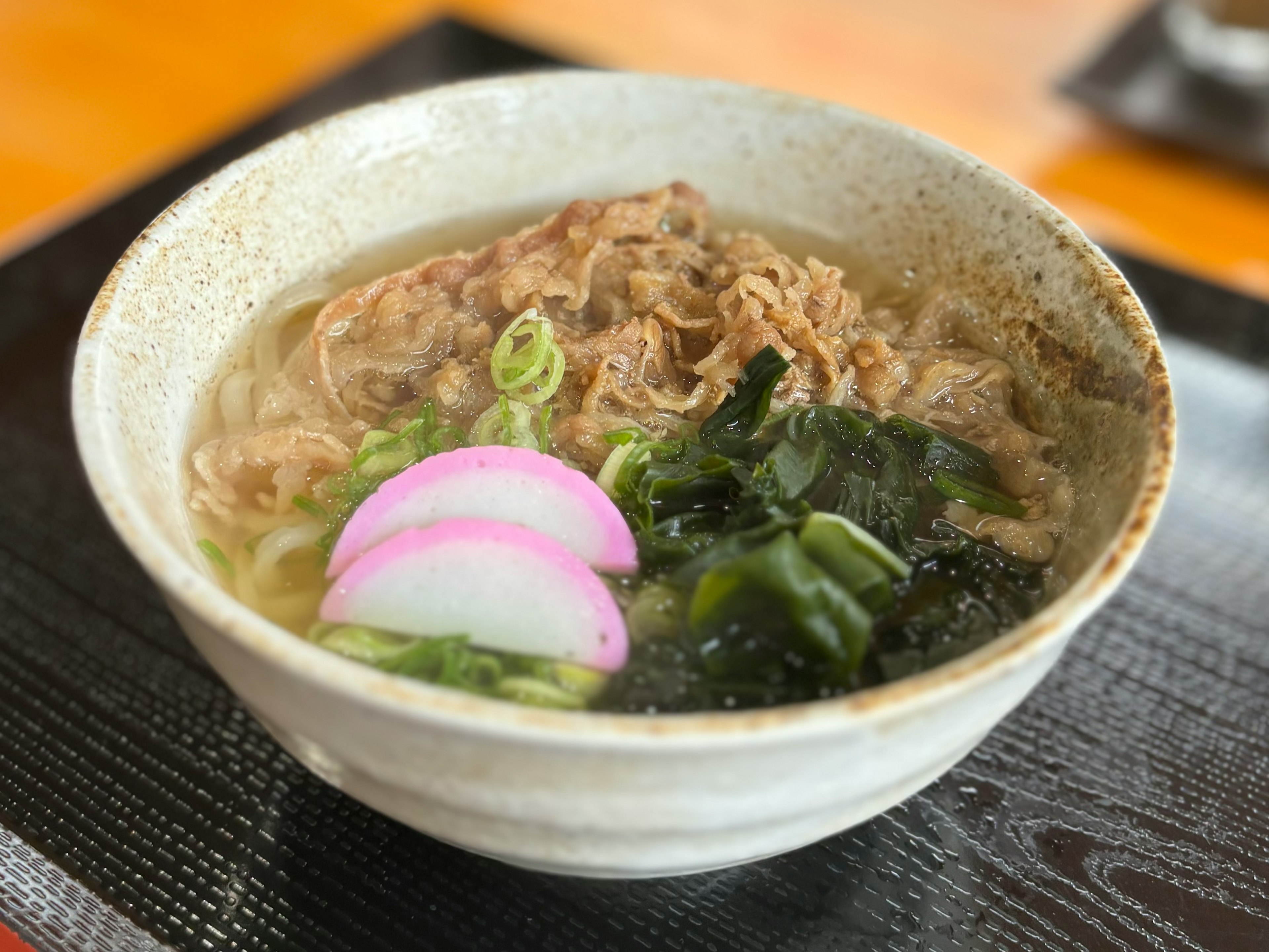 Un hermoso tazón de ramen con caldo, carne, cebollas verdes, algas y kamaboko