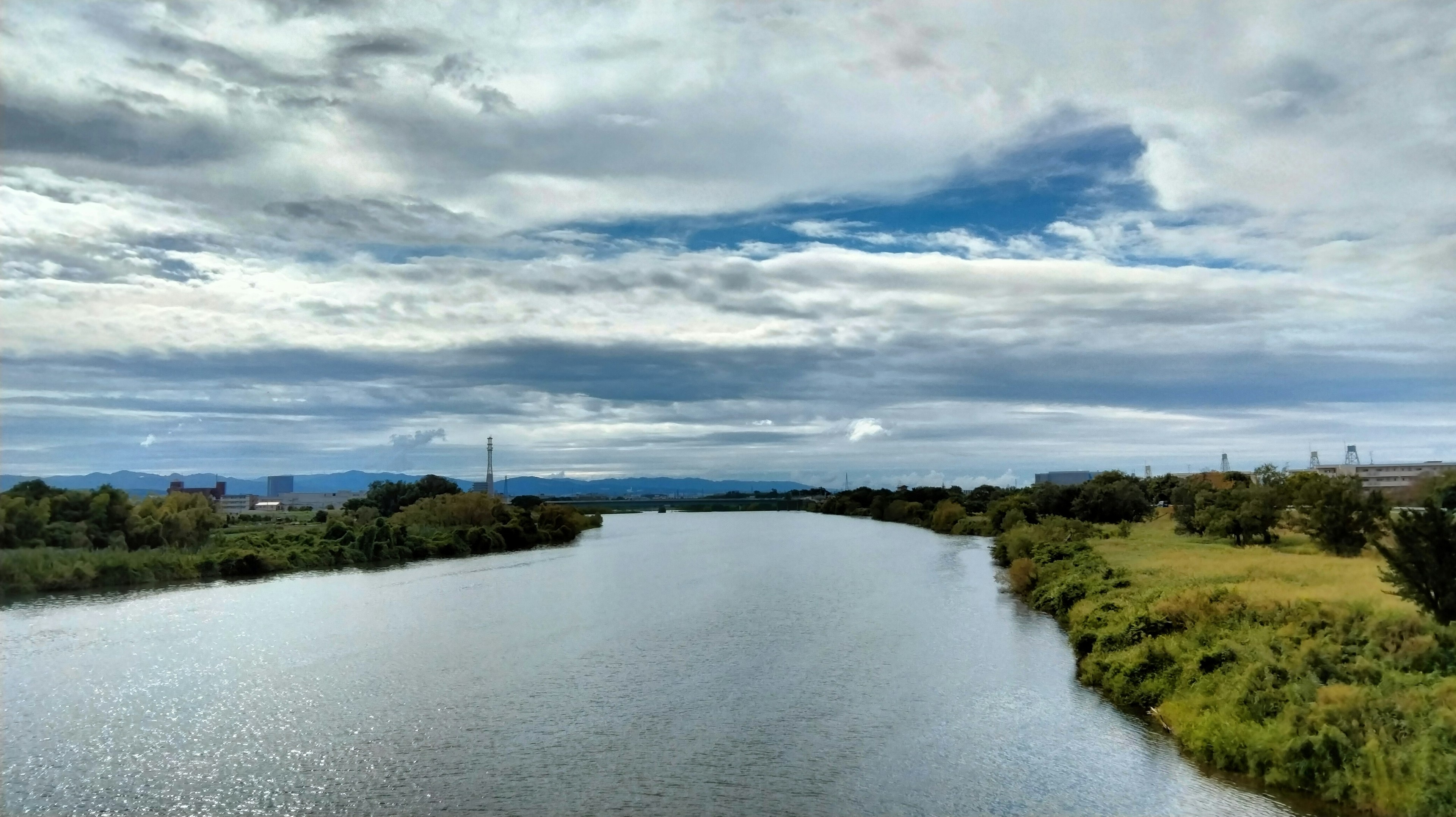 Ruhige Flusslandschaft mit weitem Himmel üppigen grünen Ufern und verstreuten Wolken