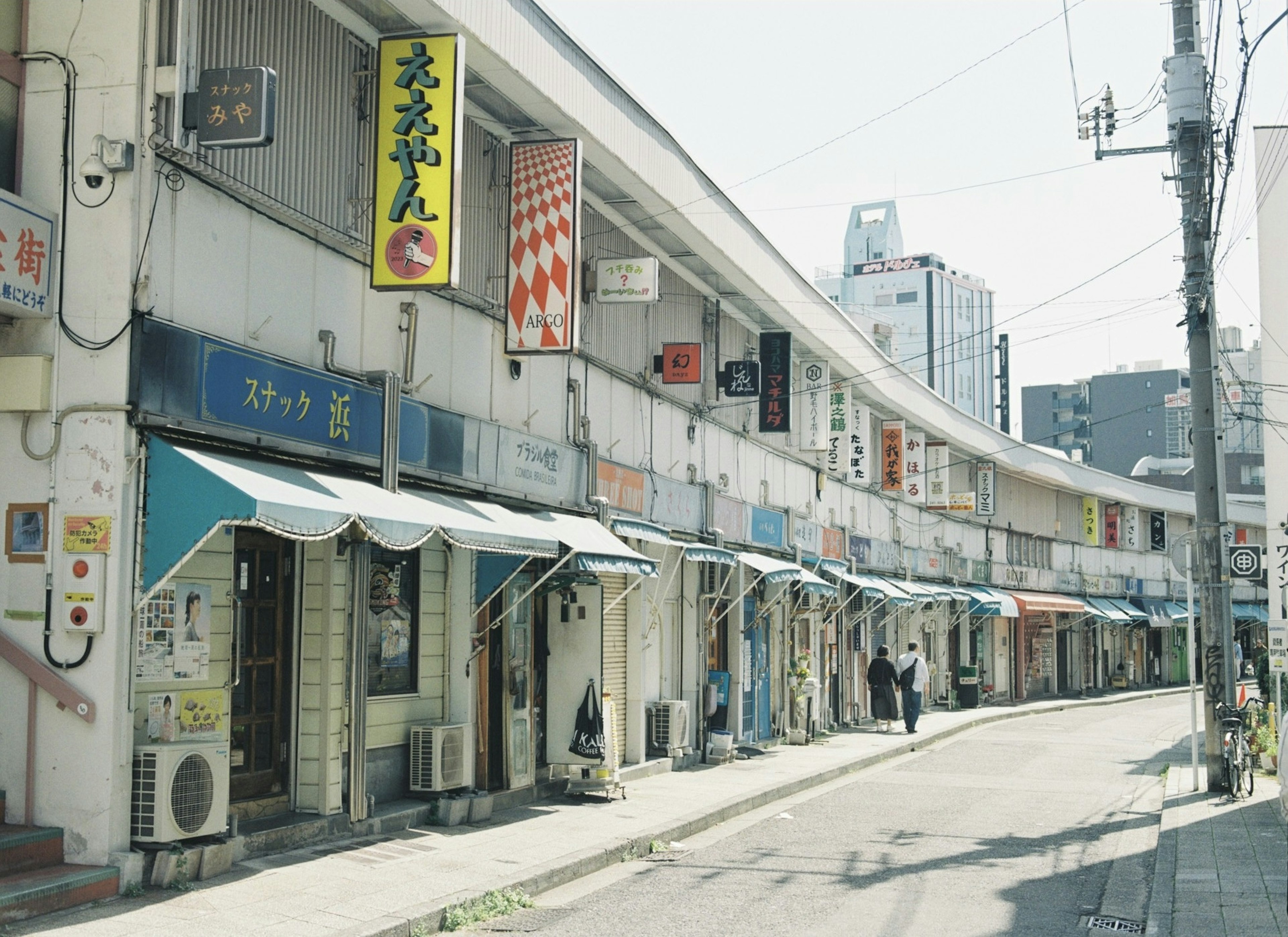 Curved street lined with shops featuring blue awnings and signs