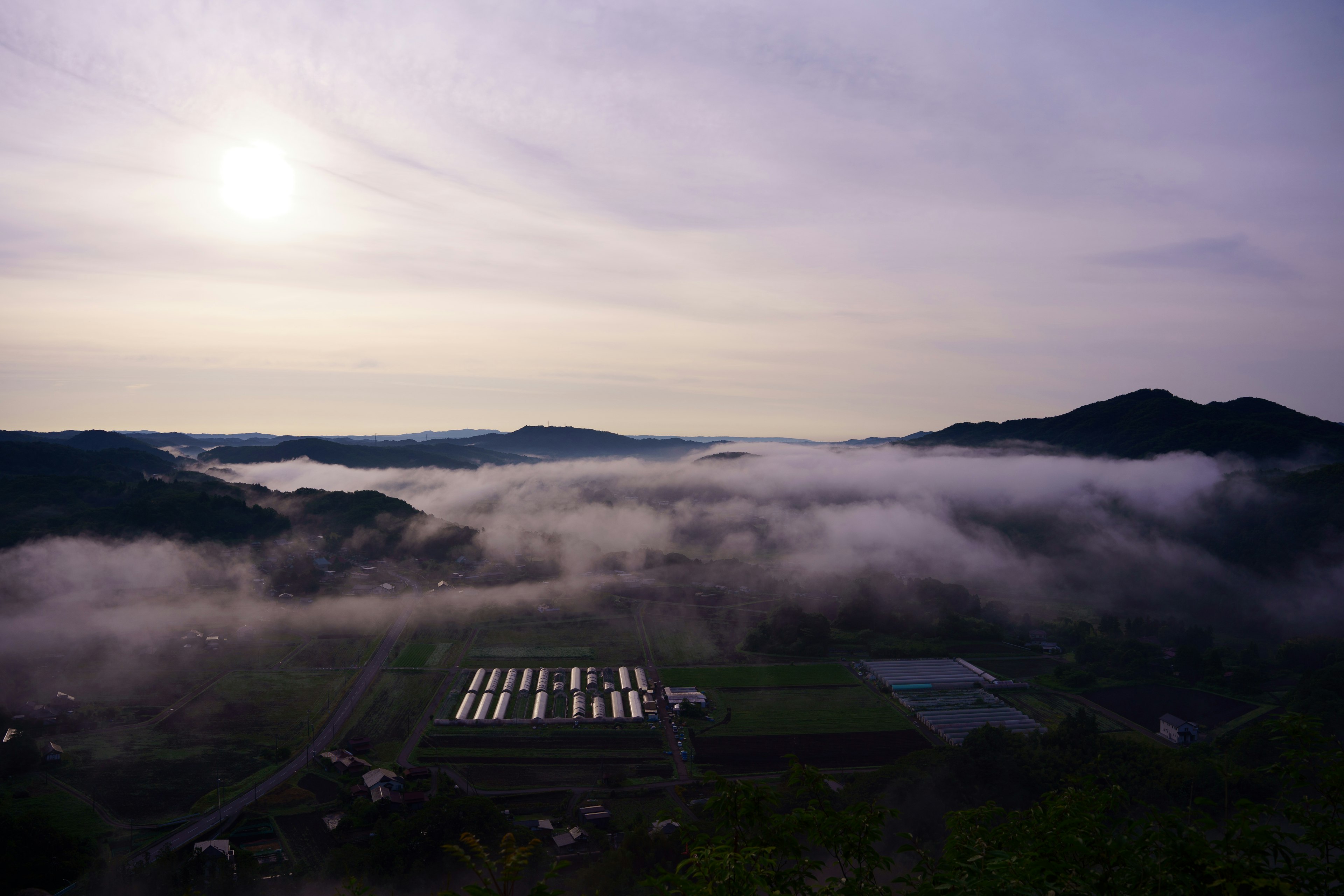 Lanskap berkabut dengan gunung dan ladang di bawah langit mendung