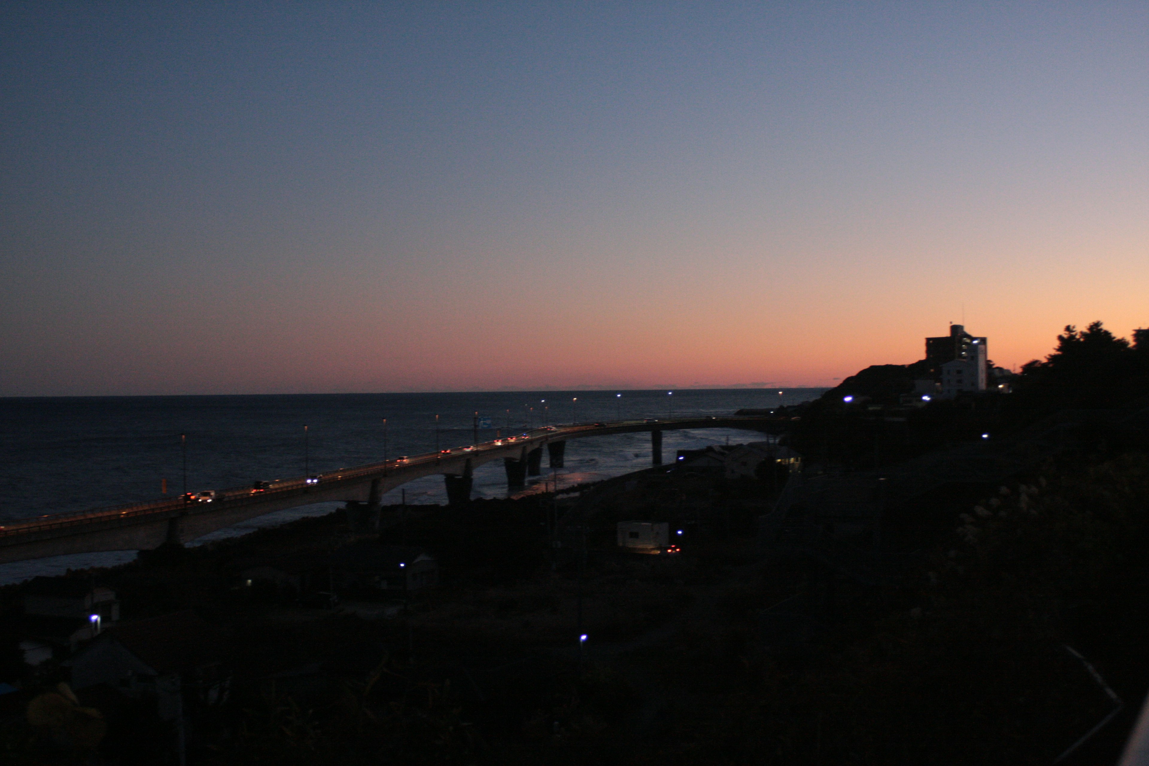 Coastal view at dusk featuring a bridge and city lights