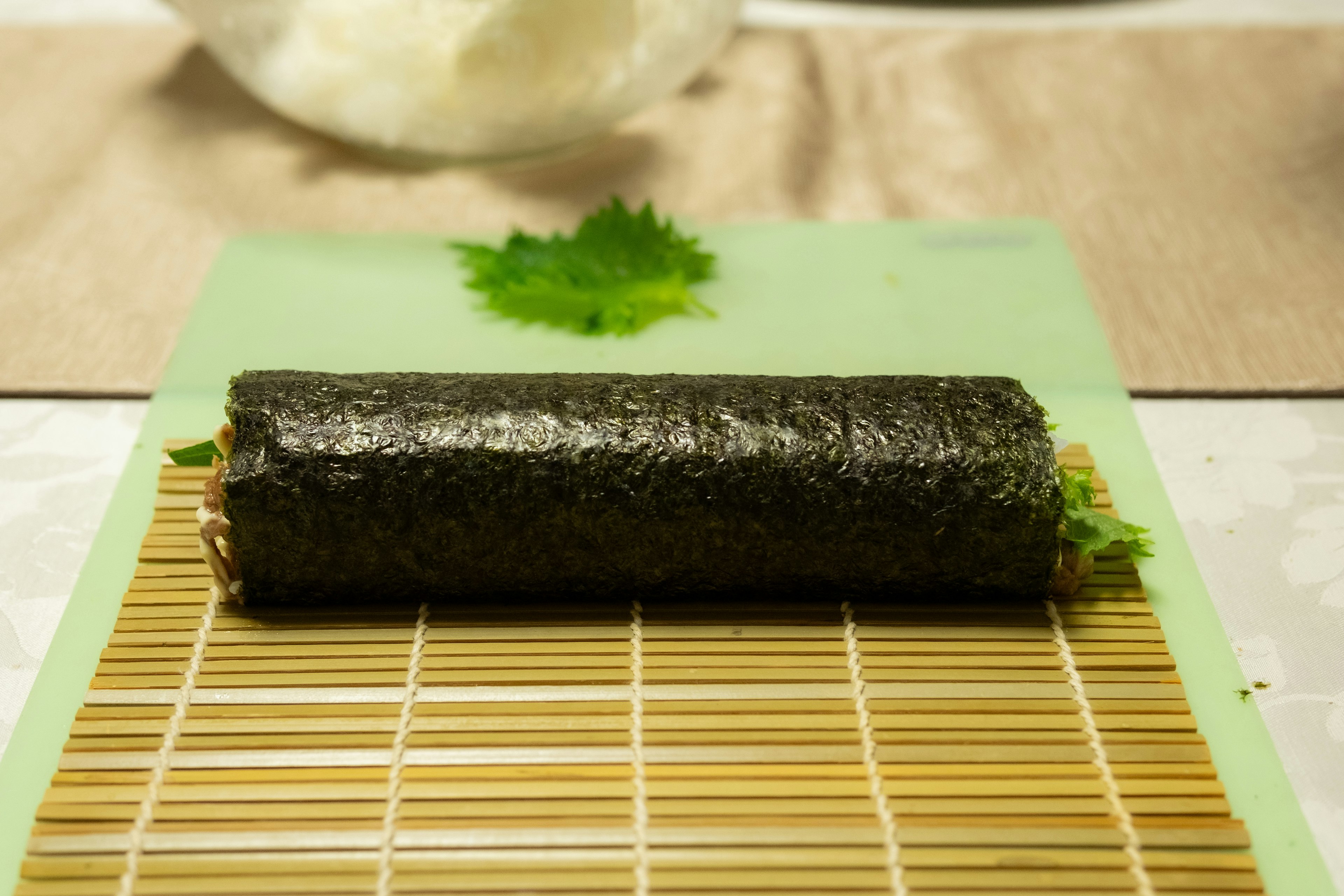 Un rollo de sushi colocado sobre una esterilla de bambú con un fondo verde