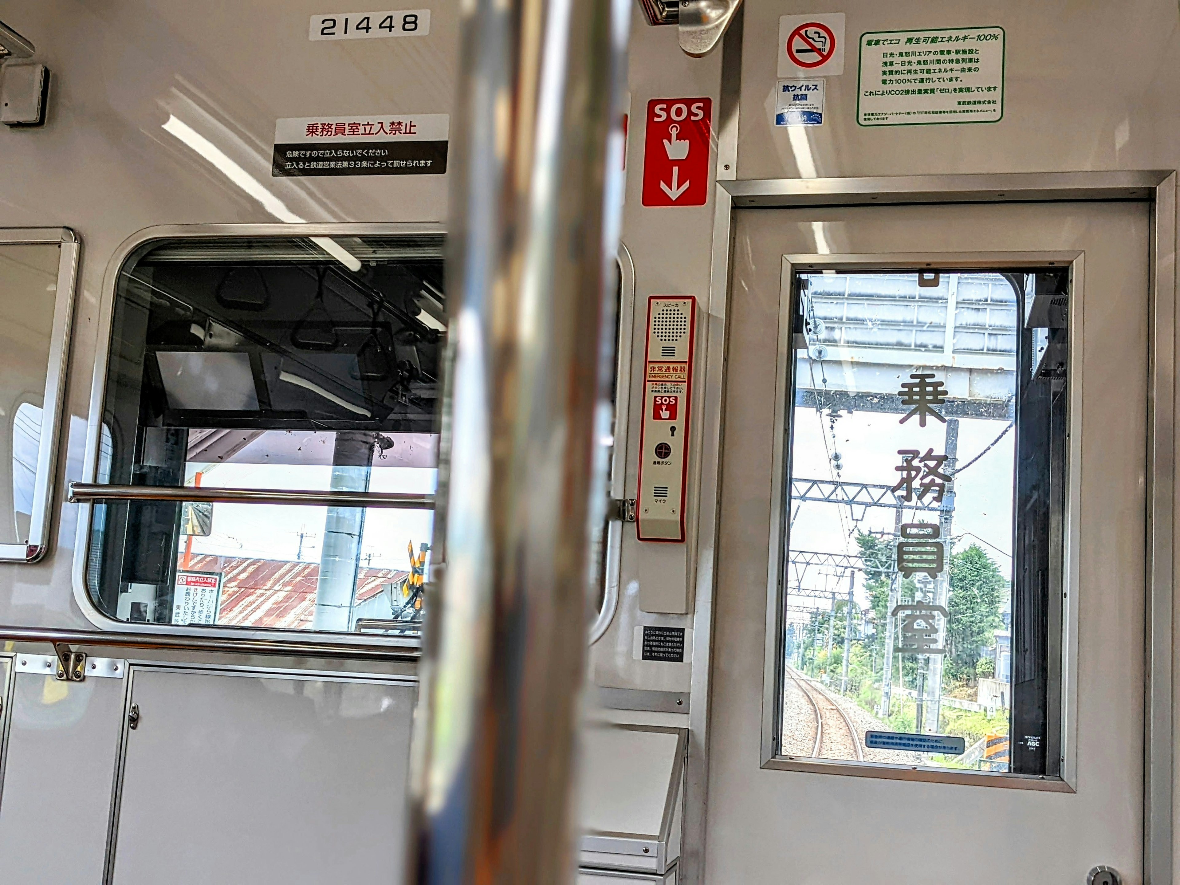 Interior view of a train showing a window and a metallic handrail with outside scenery