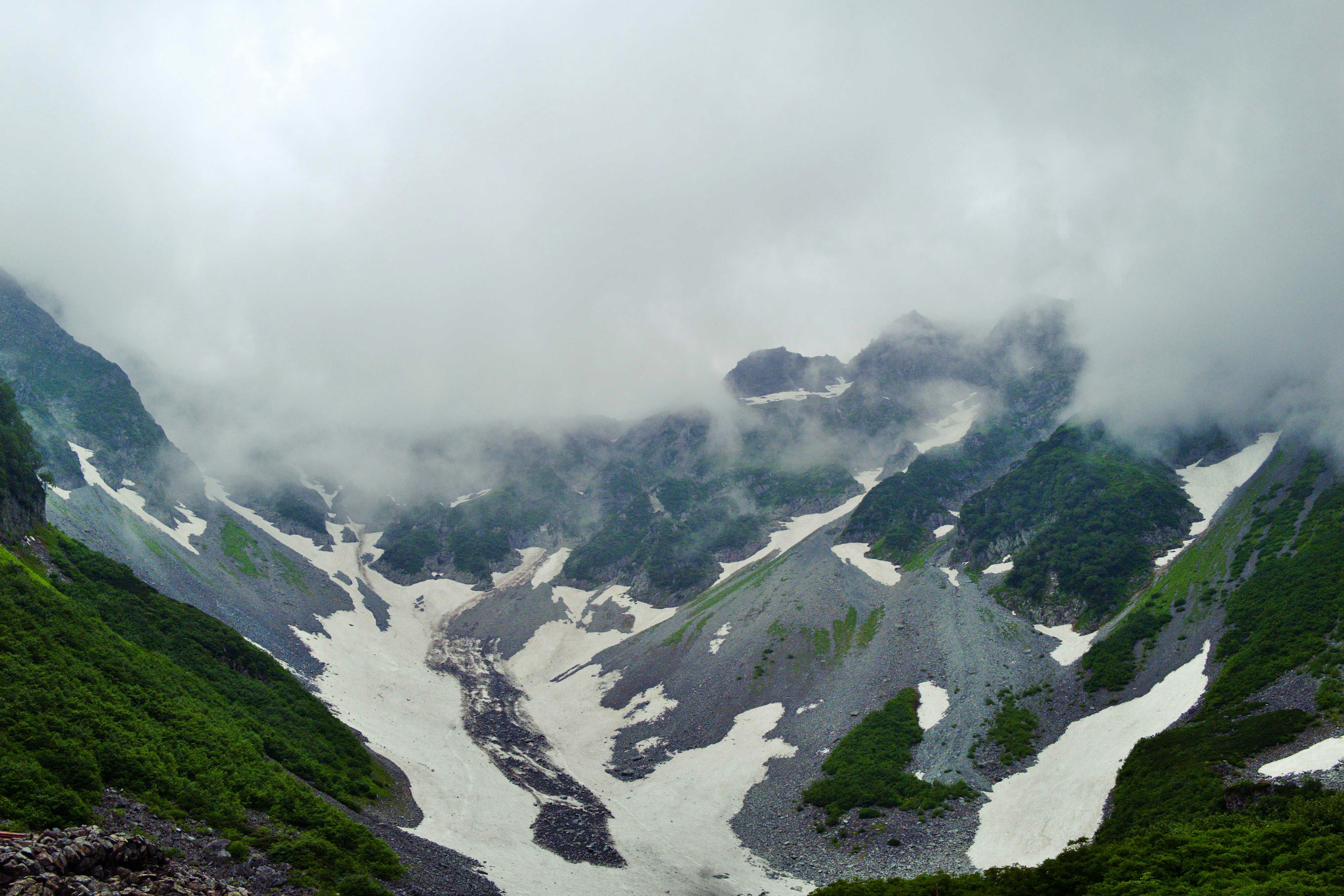 Bergtal bedeckt mit Wolken mit schmelzendem Schnee und grüner Vegetation