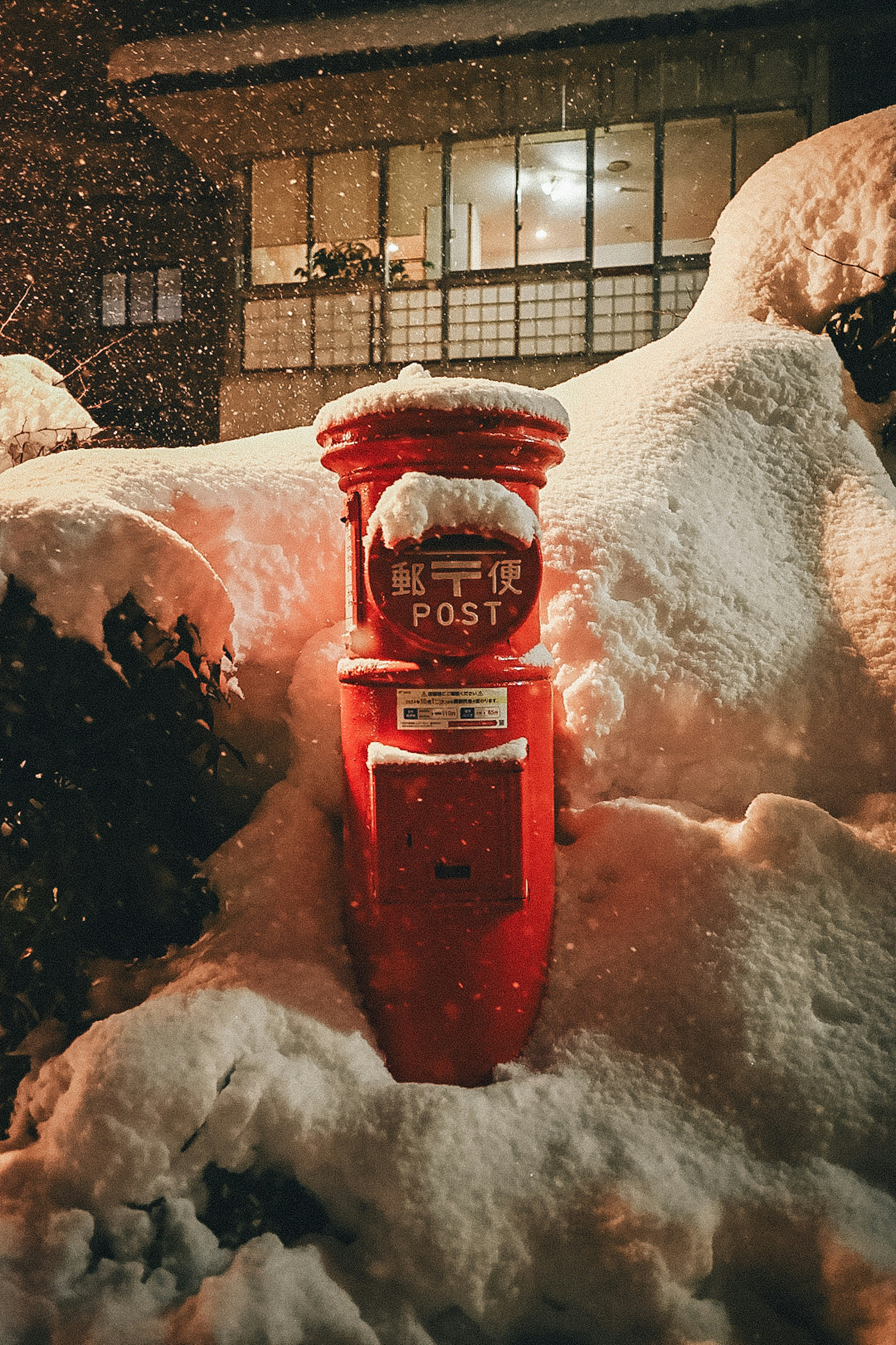 Une boîte aux lettres rouge couverte de neige avec une fenêtre de maison en arrière-plan