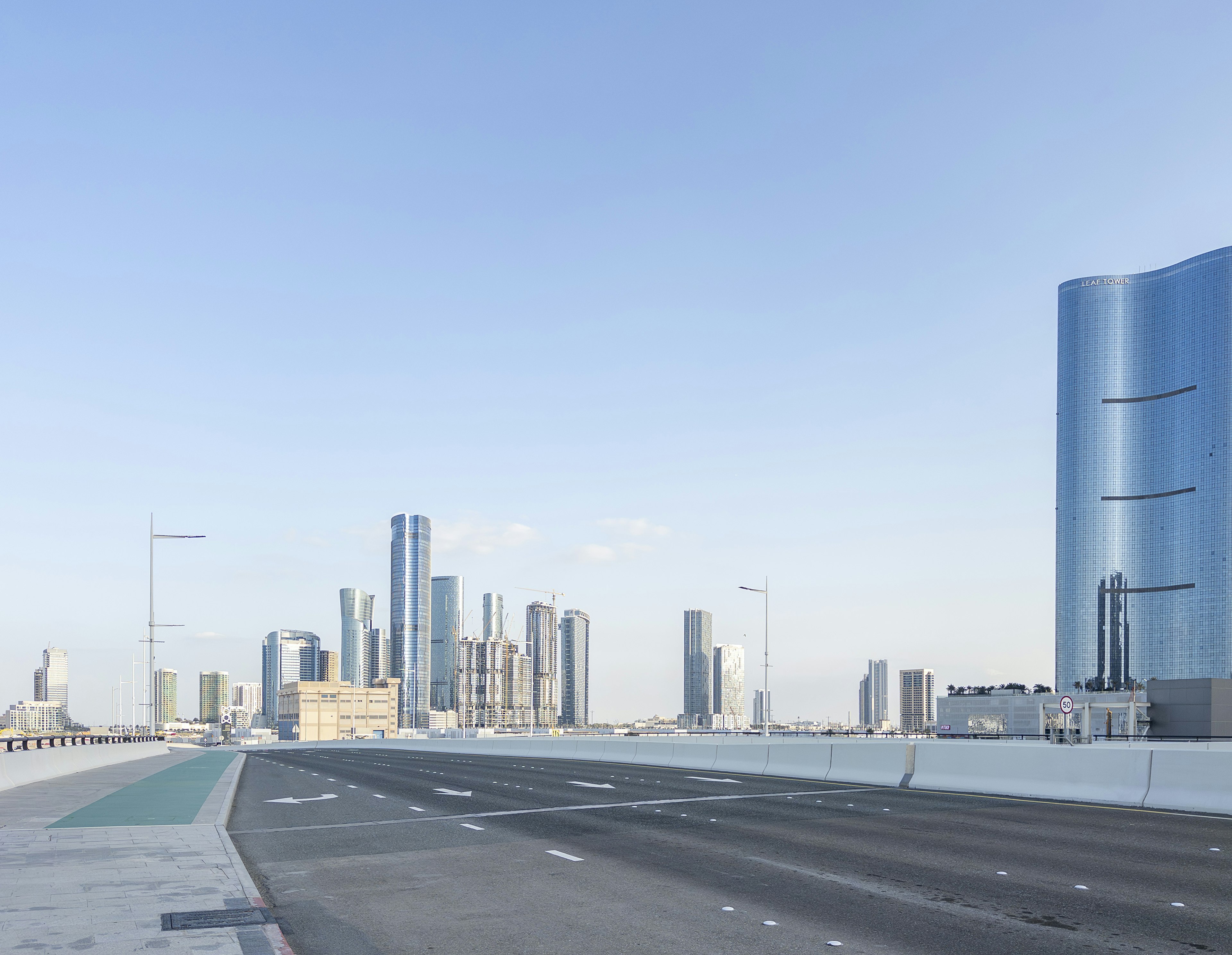 Urban landscape under a blue sky featuring skyscrapers and an empty road