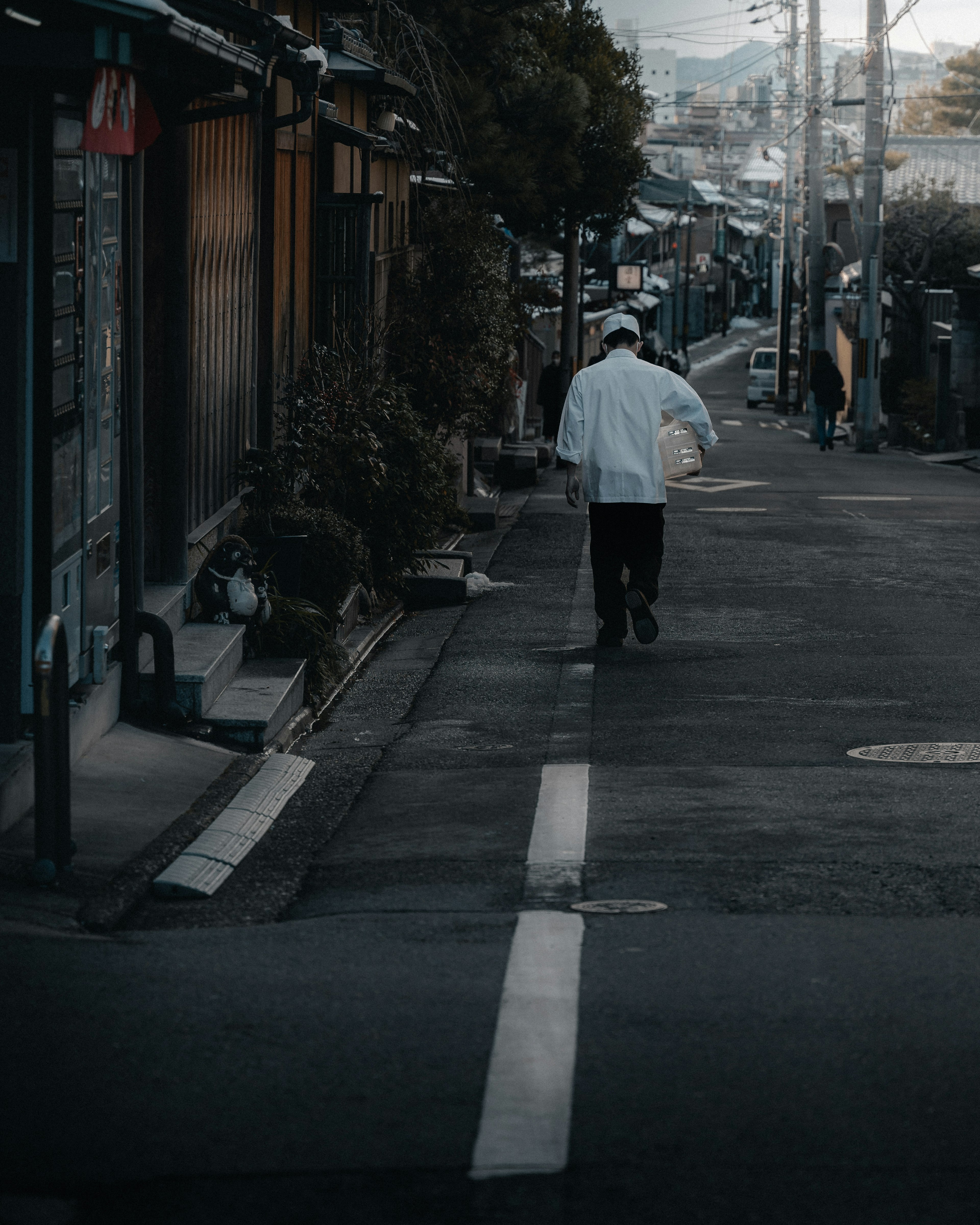 A man in white clothing walking down a quiet street