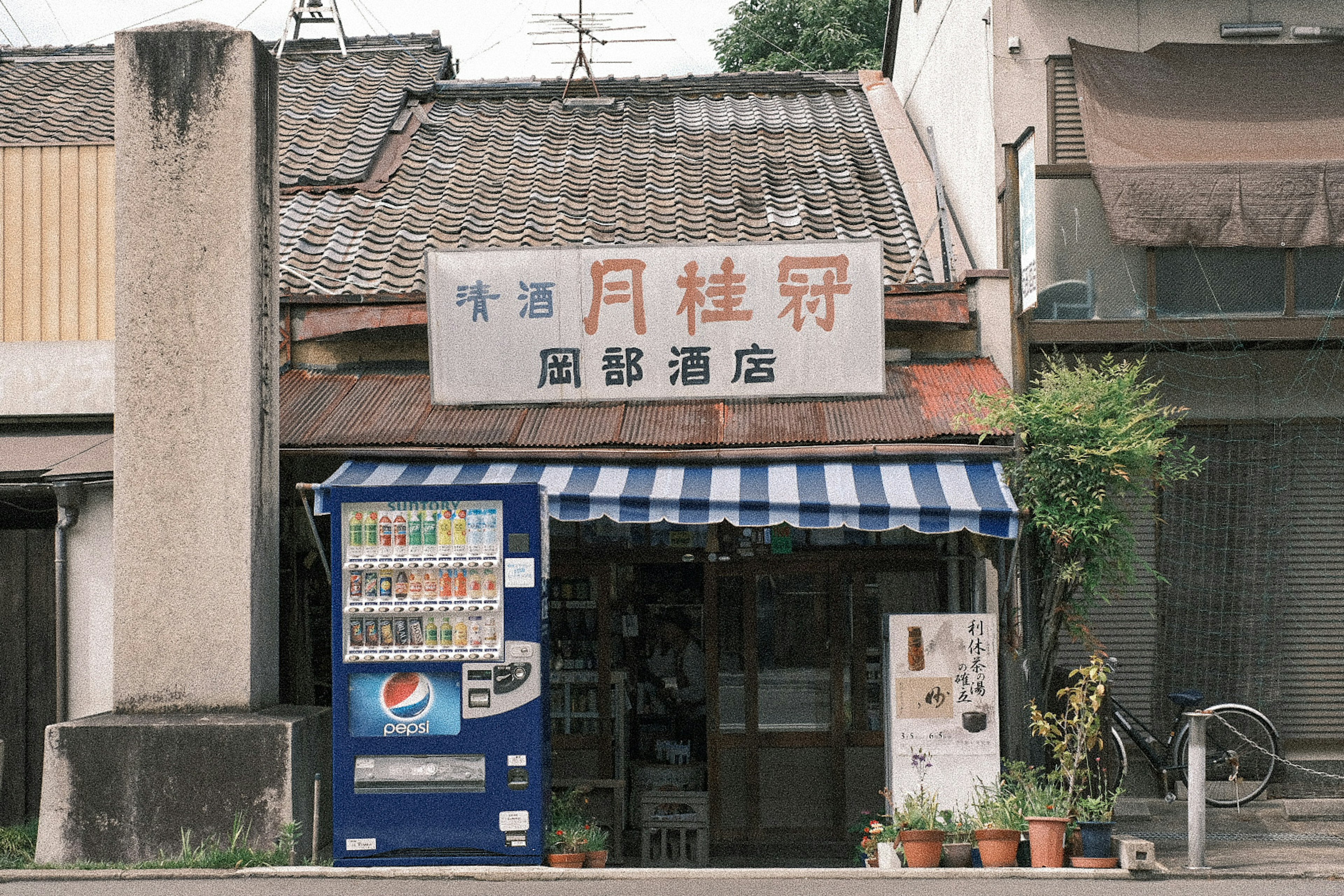 Exterior of an old shop featuring a blue and white striped awning with a vending machine