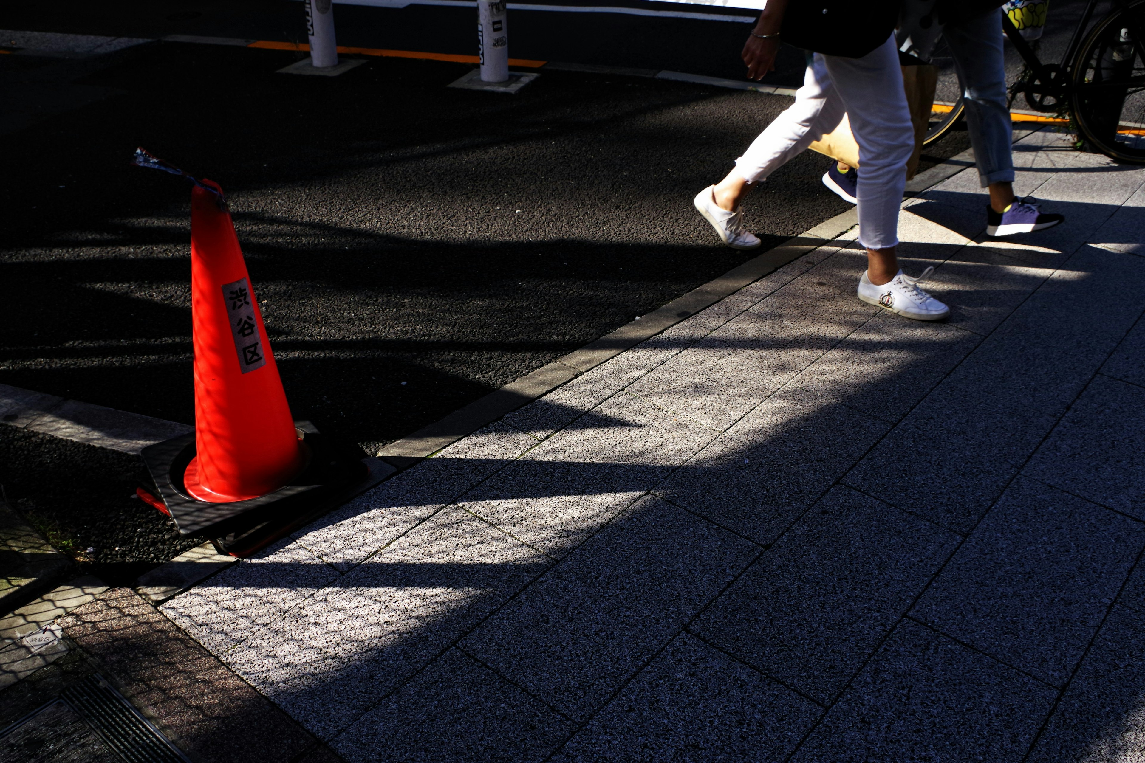 Urban scene with a red cone and shadows of pedestrians