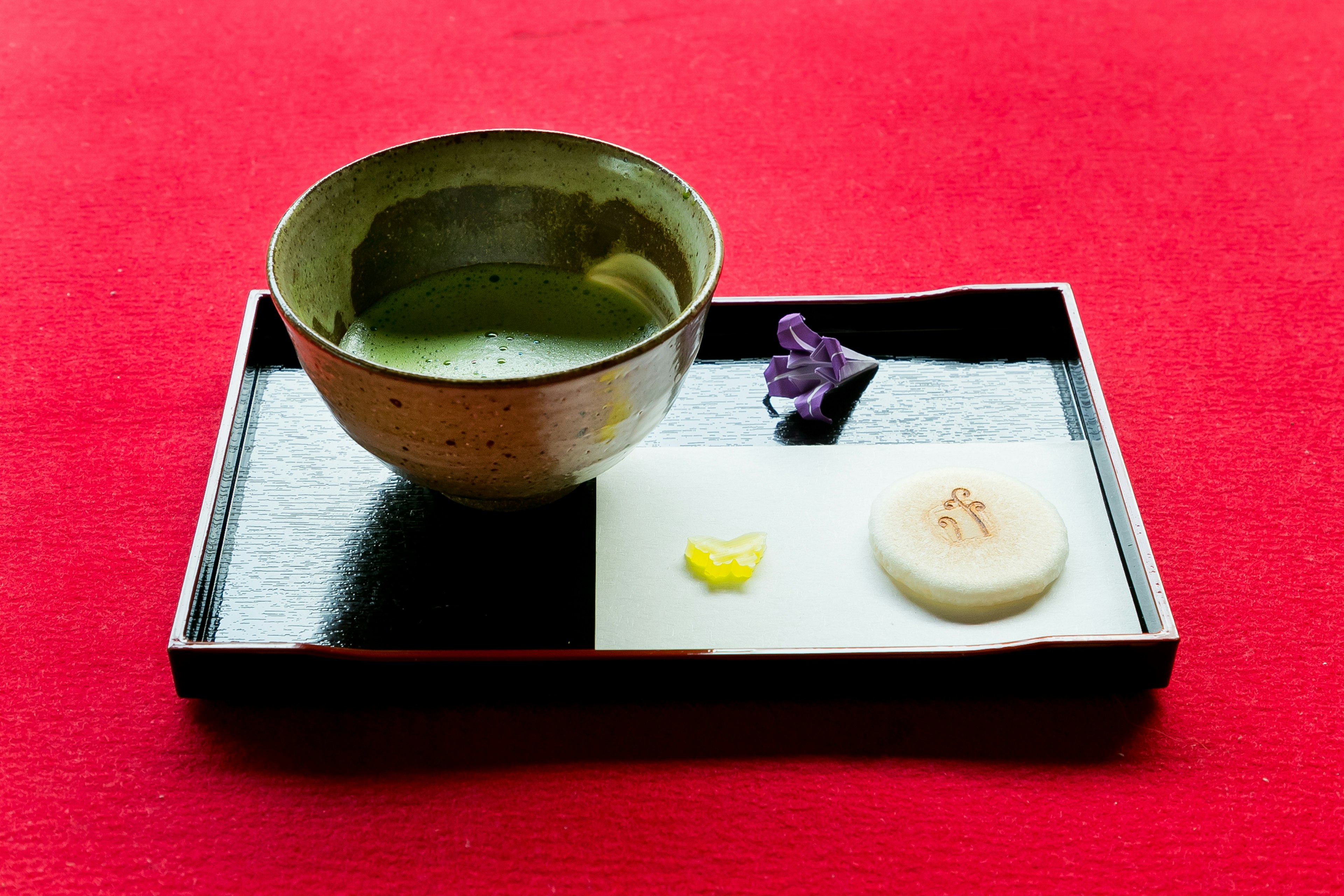 Matcha tea bowl with wagashi on a black tray red background