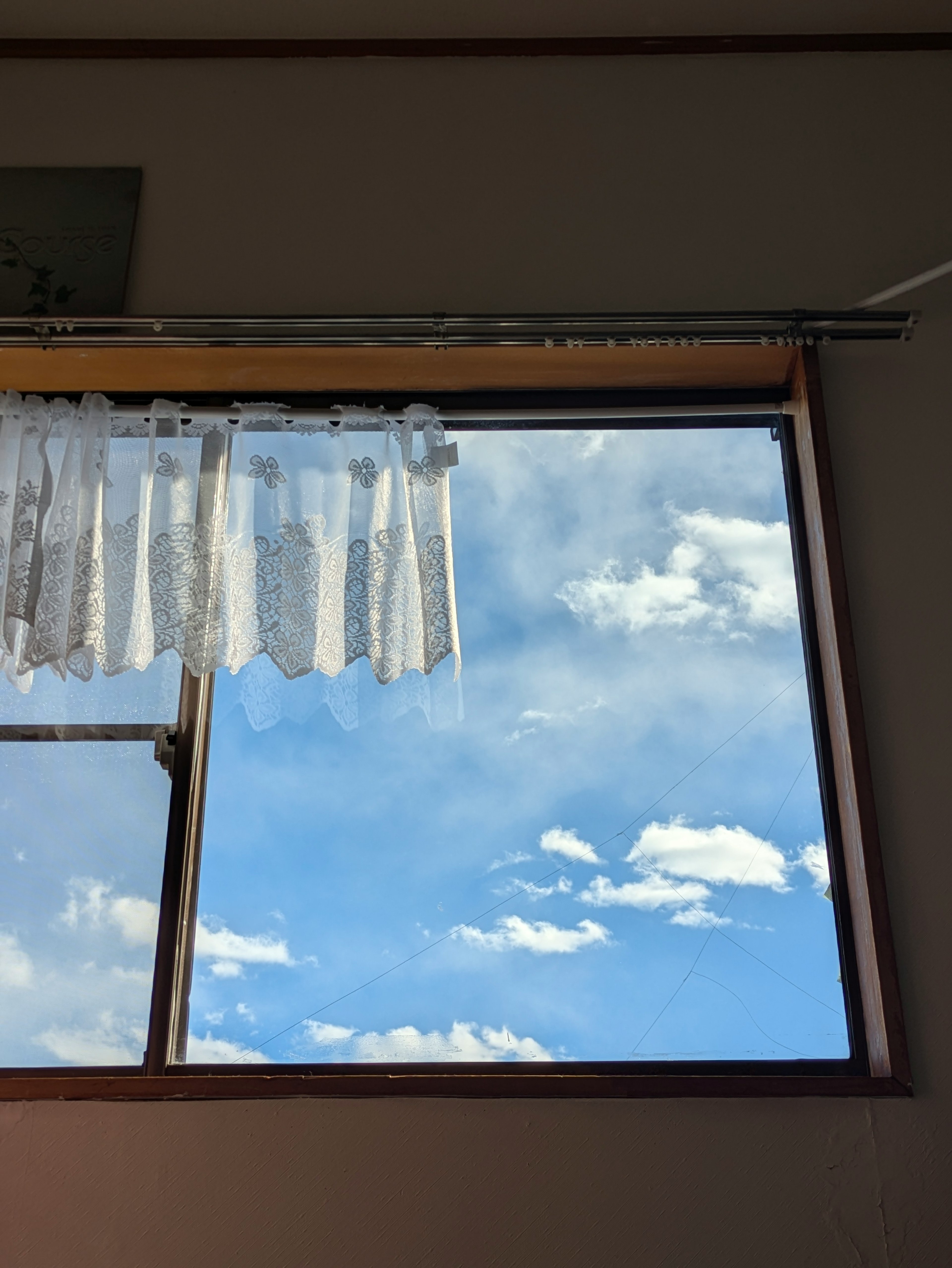 Finestra con tende bianche che mostrano un cielo blu e nuvole bianche