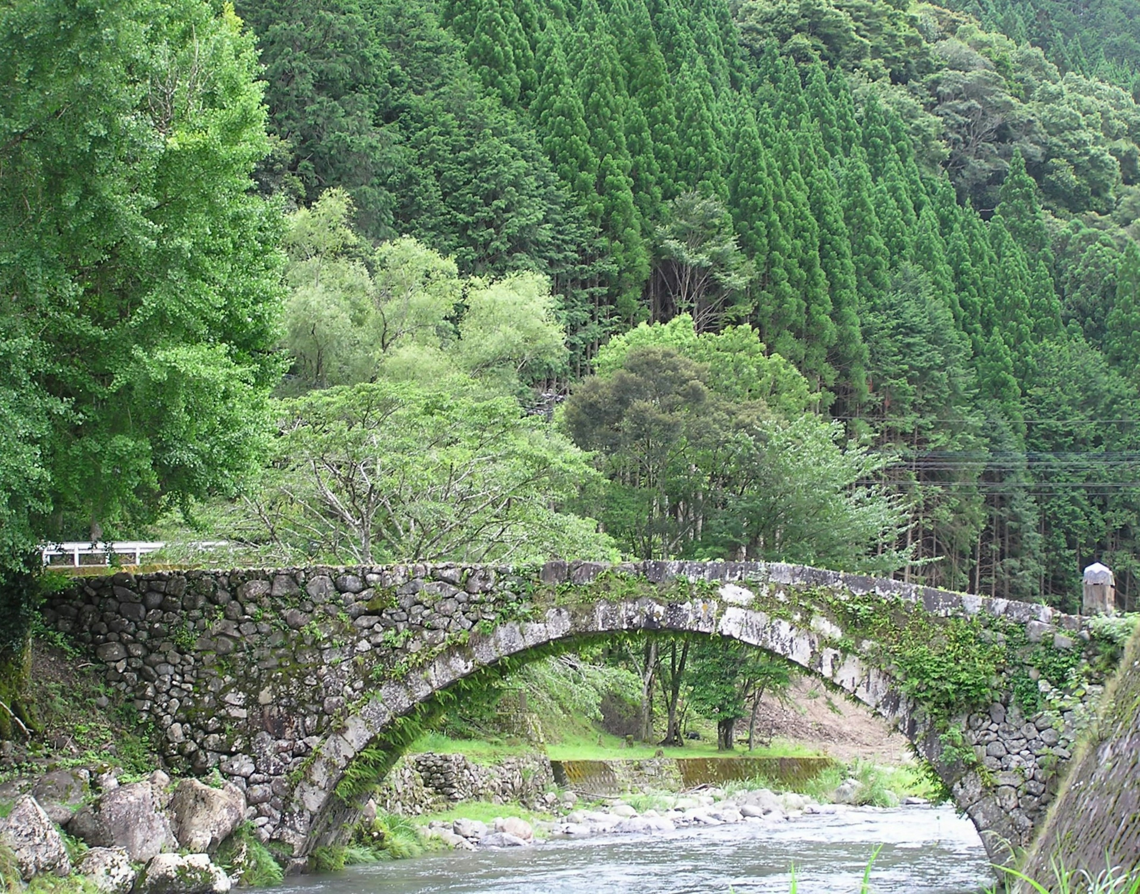 Puente de piedra en arco rodeado de montañas verdes y un arroyo claro