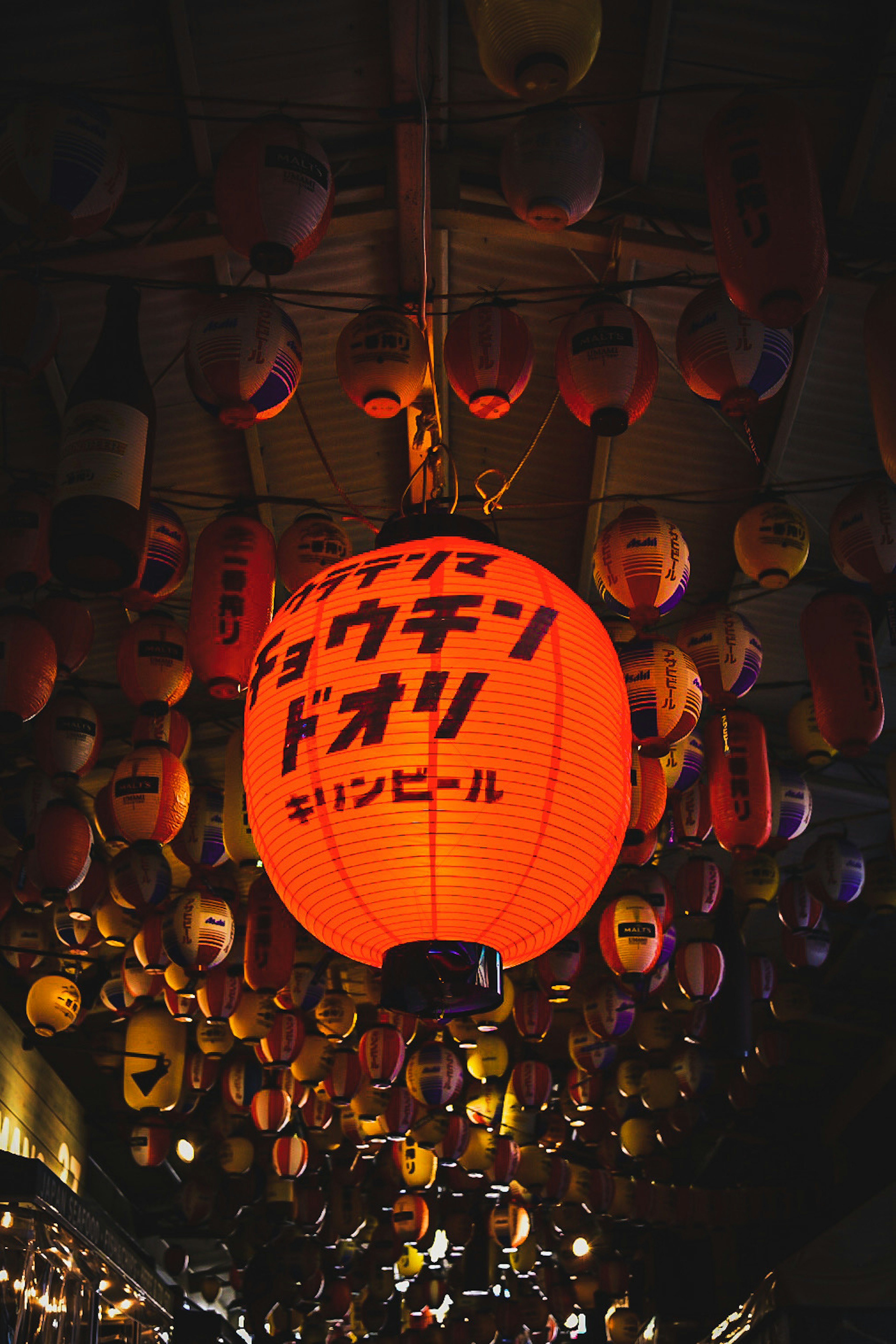 Scène intérieure avec des lanternes colorées suspendues au plafond mettant en avant une grande lanterne orange