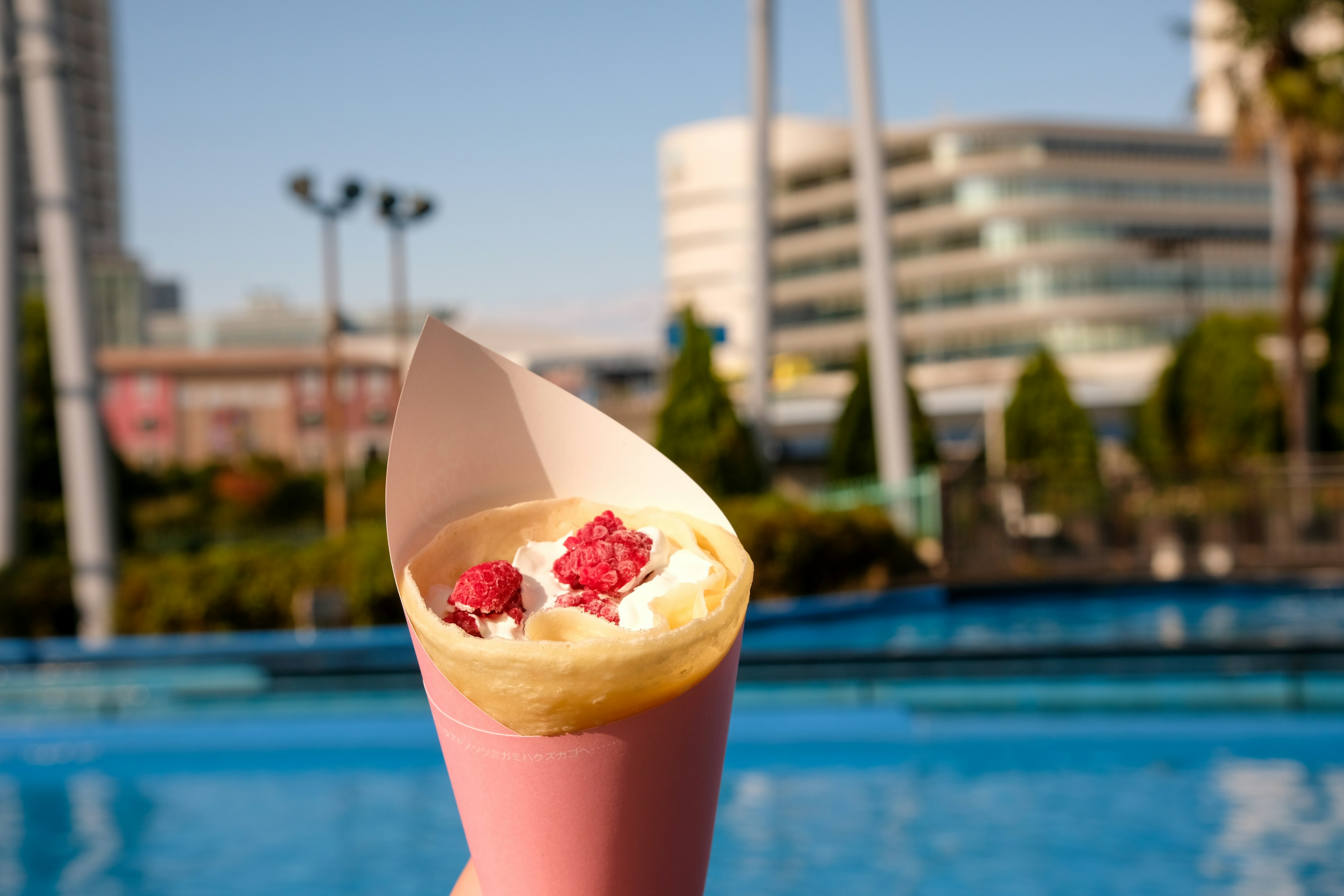 Eine rosa Crêpe gefüllt mit Schlagsahne und Himbeeren vor einem sonnigen Hintergrund