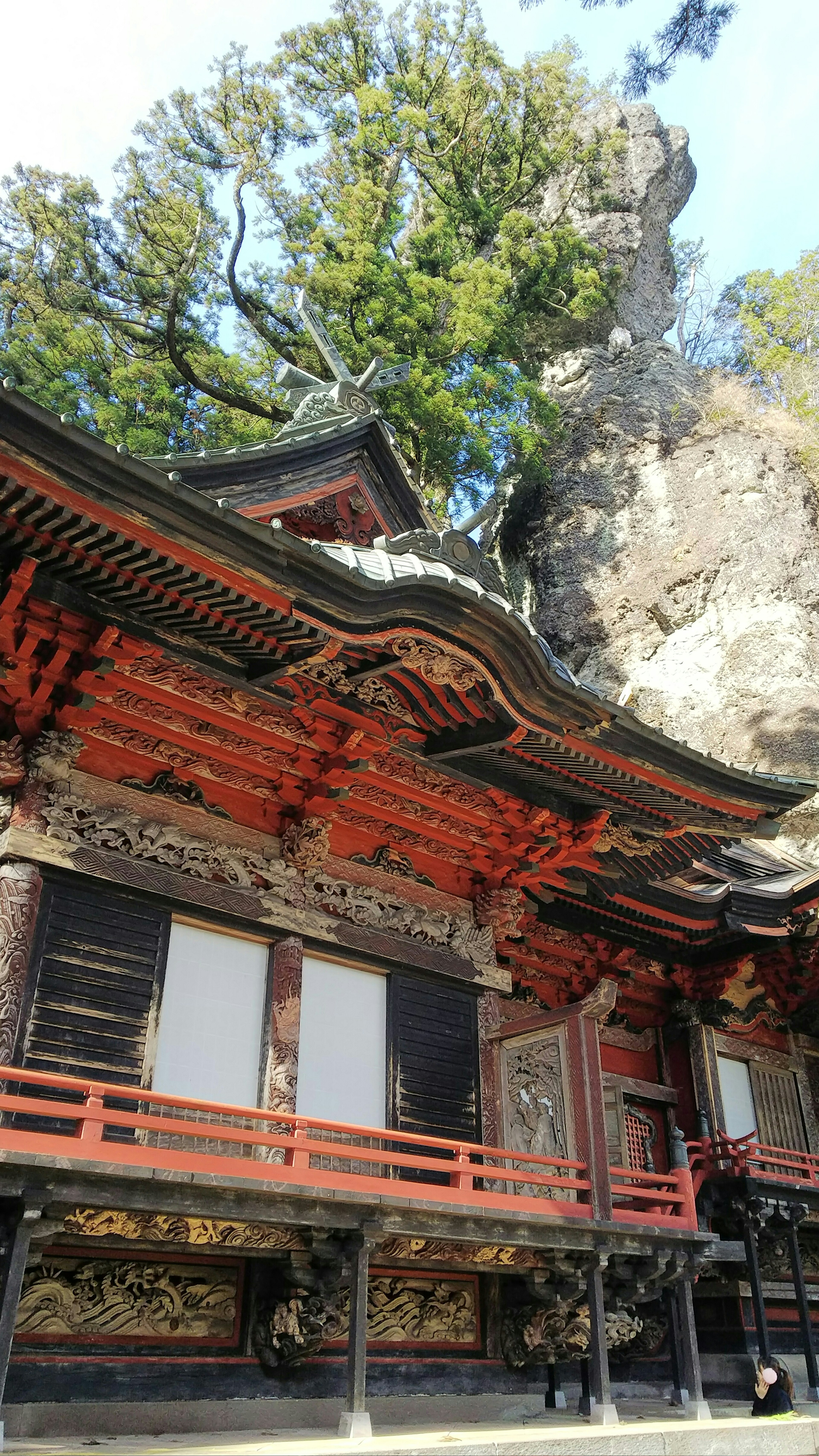 红色历史寺庙建筑位于岩石悬崖旁，四周环绕着绿色树木