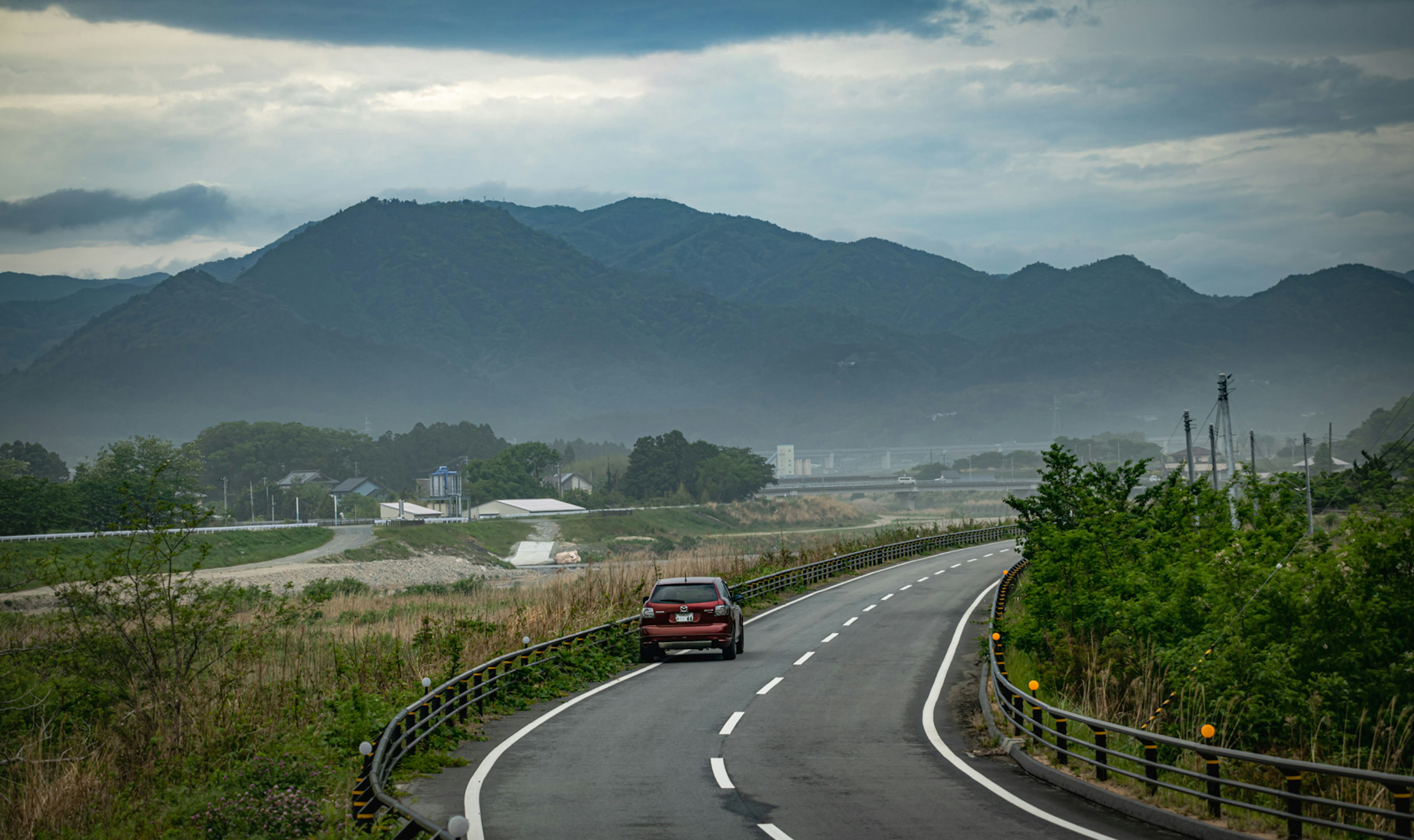 緑豊かな道路を走る赤い車と遠くの山々