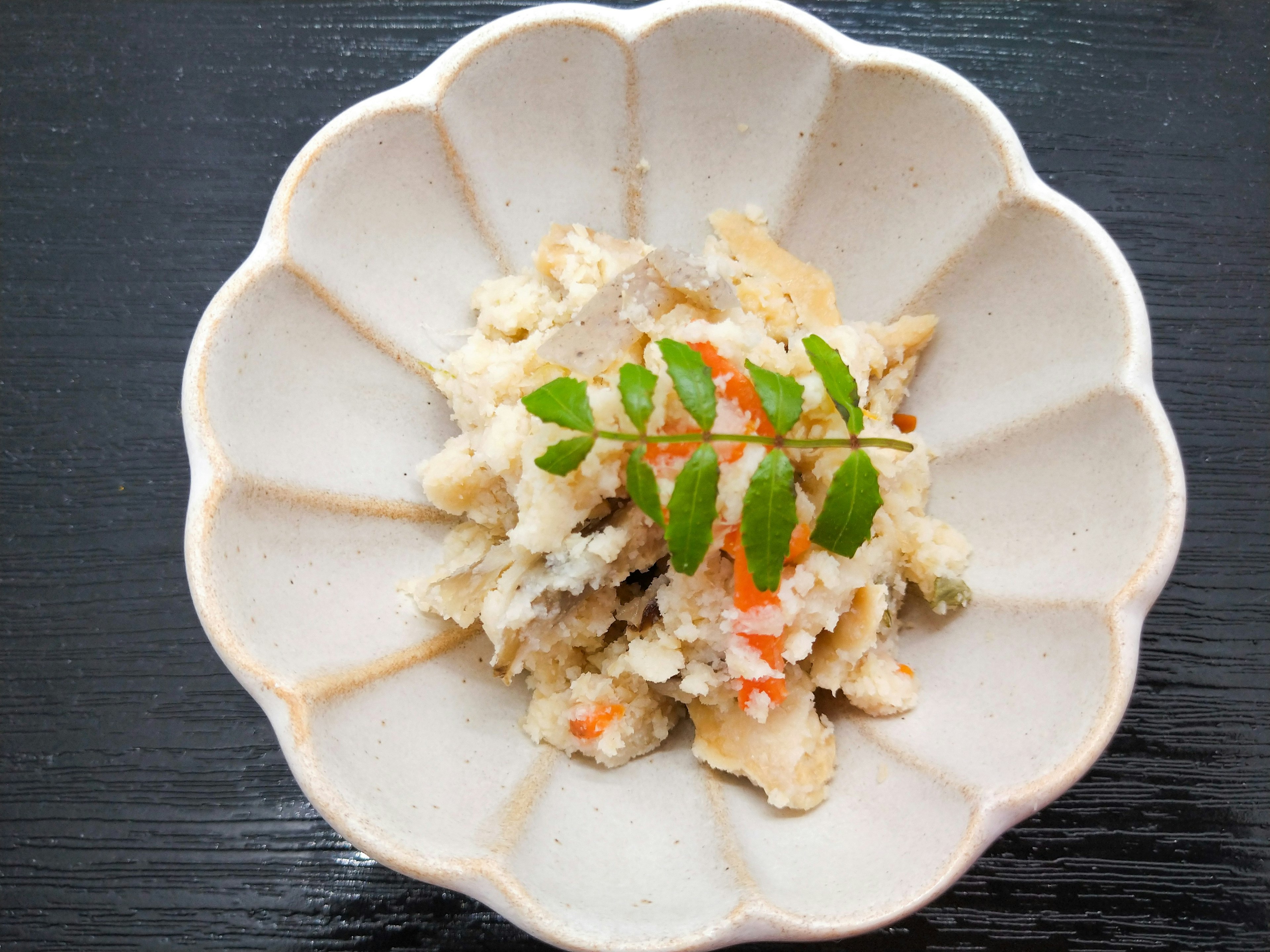 Plat japonais servi dans une assiette blanche poisson haché et légumes mélangés surmontés de feuilles vertes