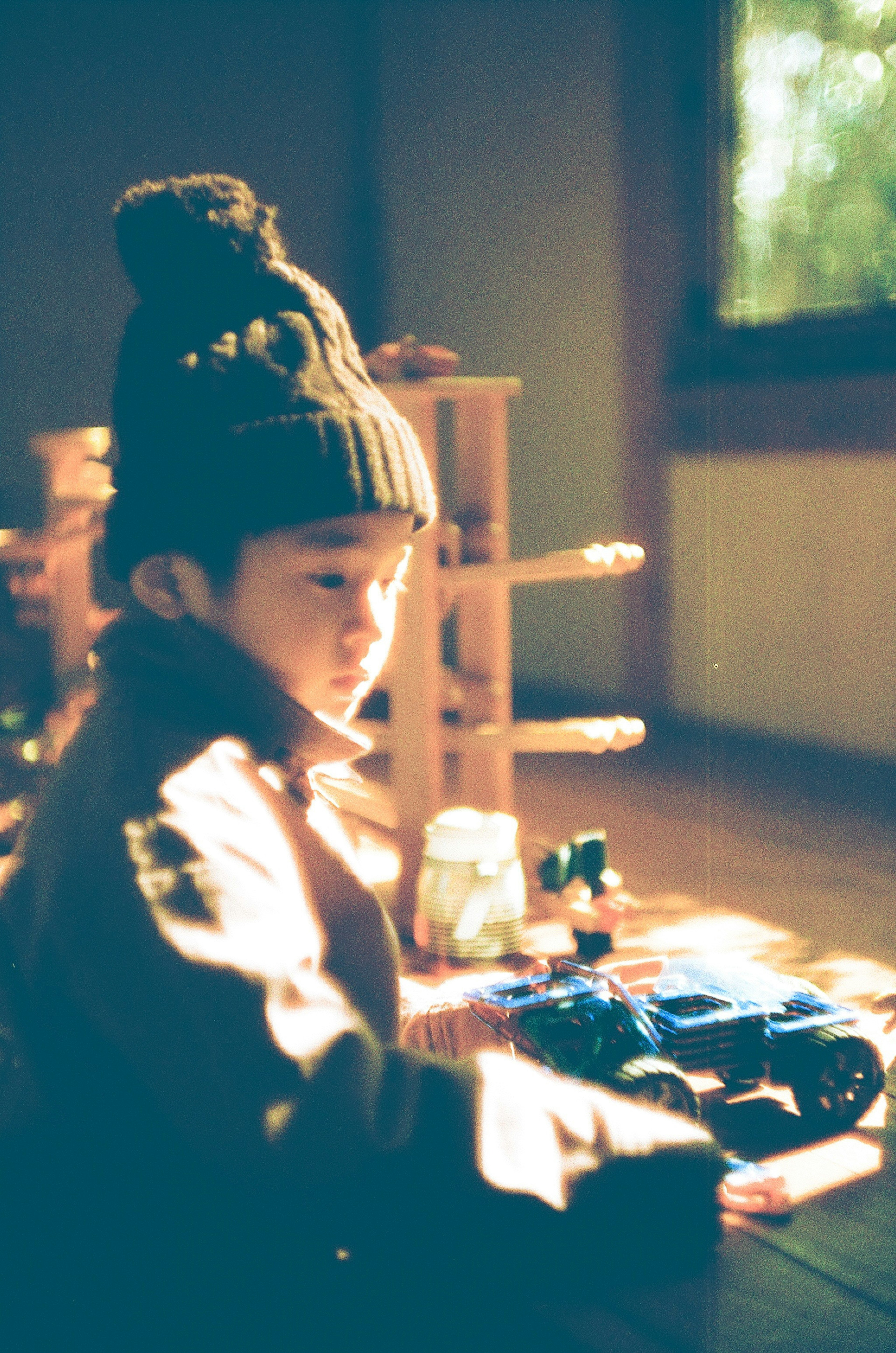 A child playing with wooden toys wearing a knitted hat in a softly lit room