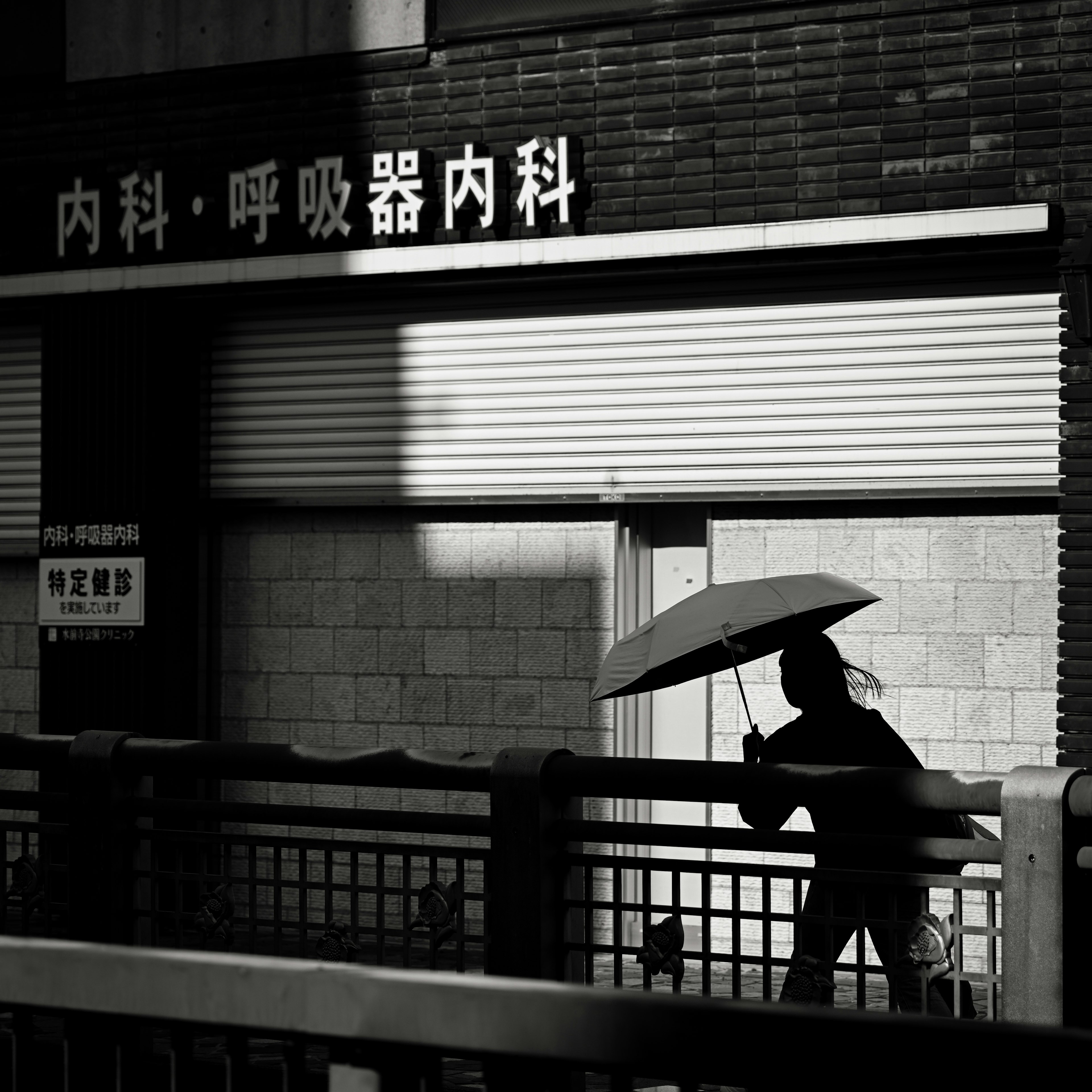 Silhouette of a person walking with an umbrella in front of a shop sign