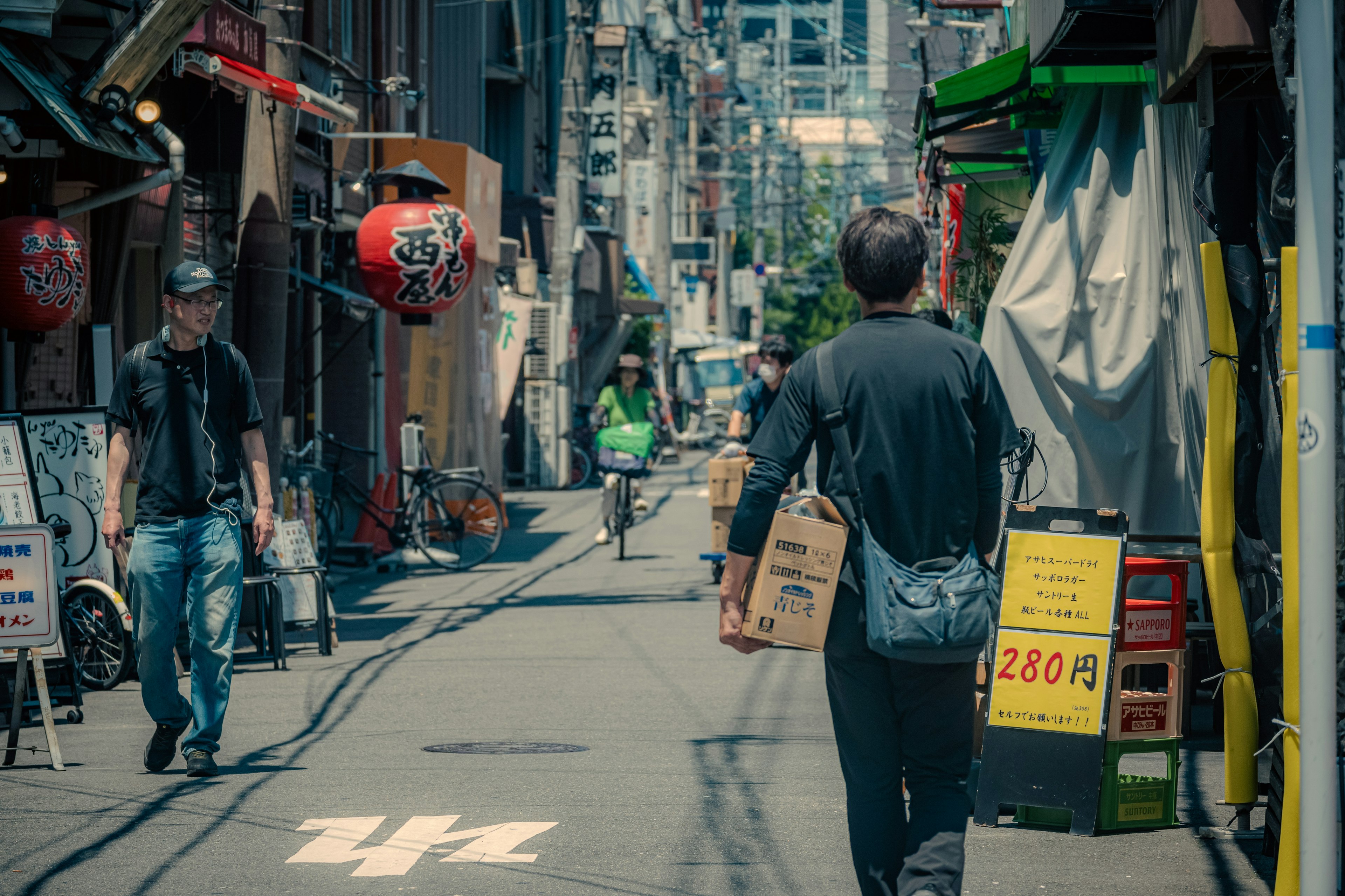 狭い路地を歩く男性と店舗の看板が見える街の風景