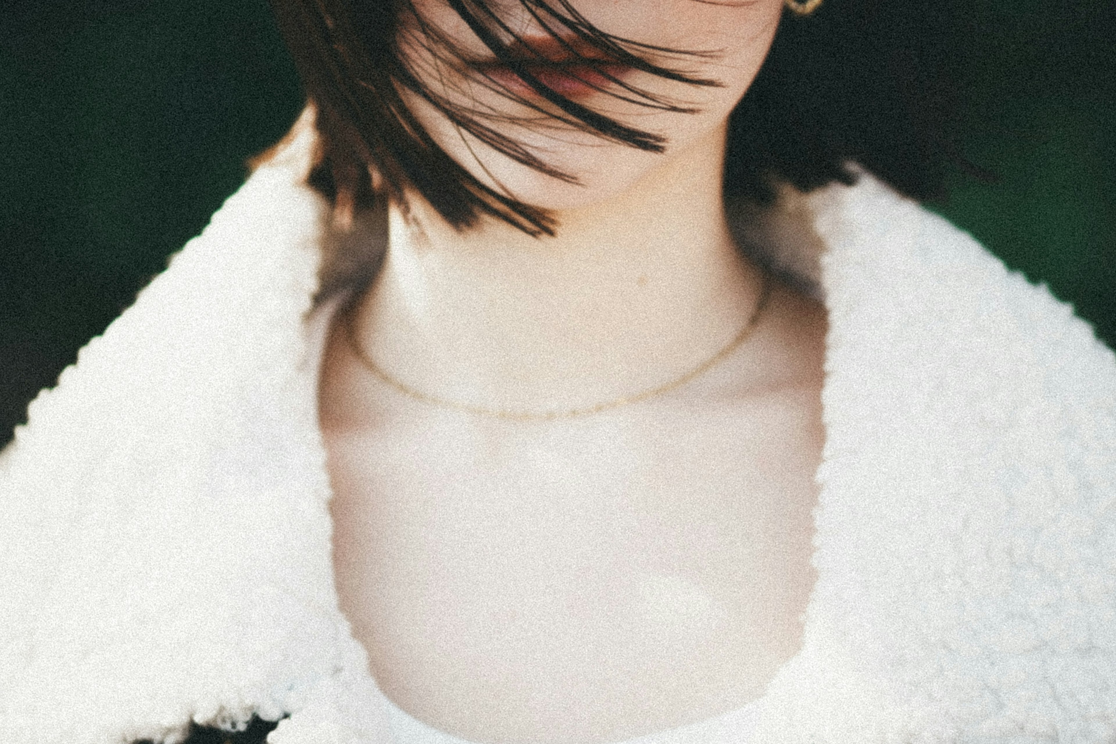 Primo piano di una donna con capelli mossi dal vento che indossa un cappotto bianco