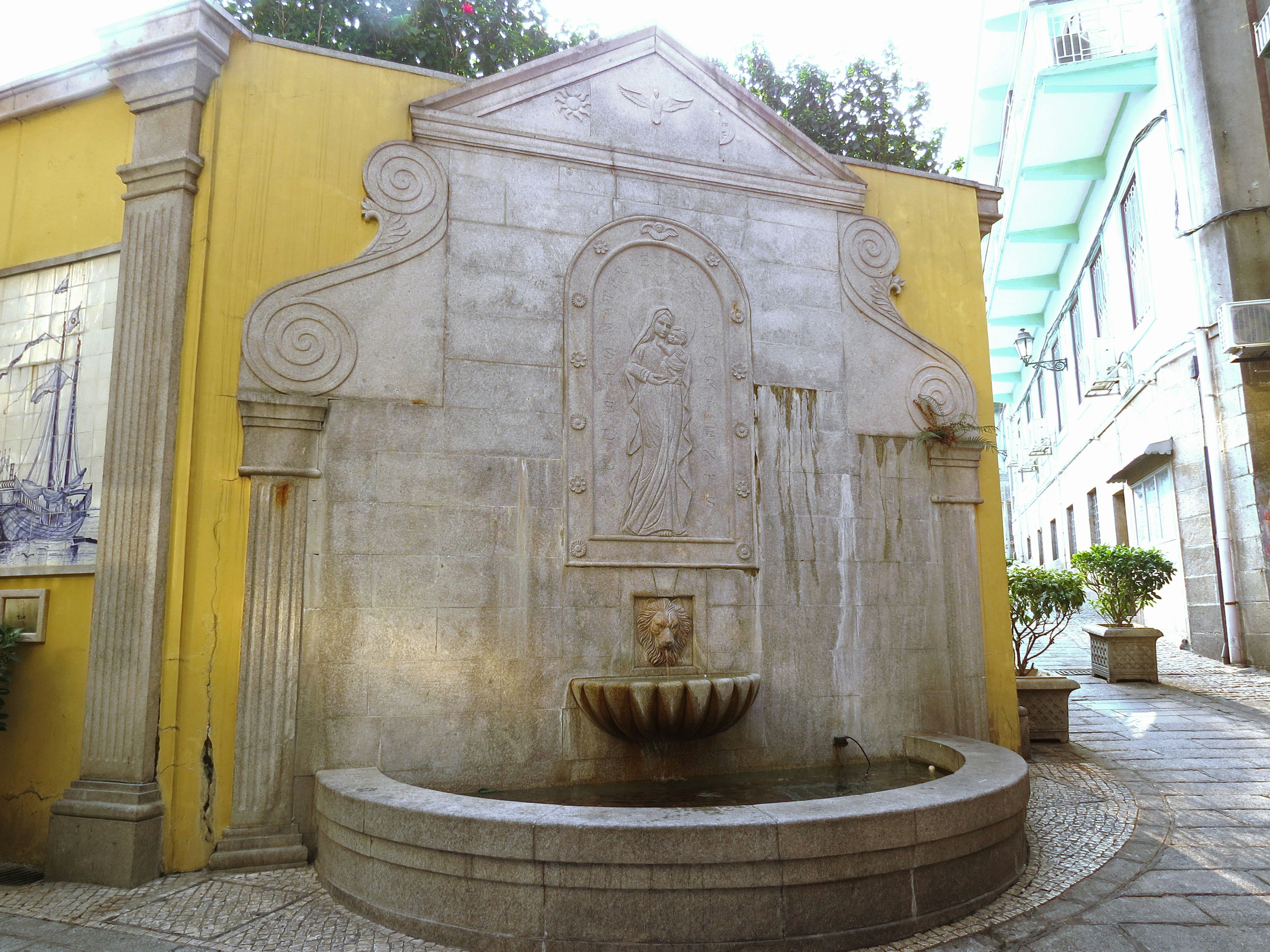 Hermosa fuente de piedra en un jardín con intrincadas tallas y una pared amarilla