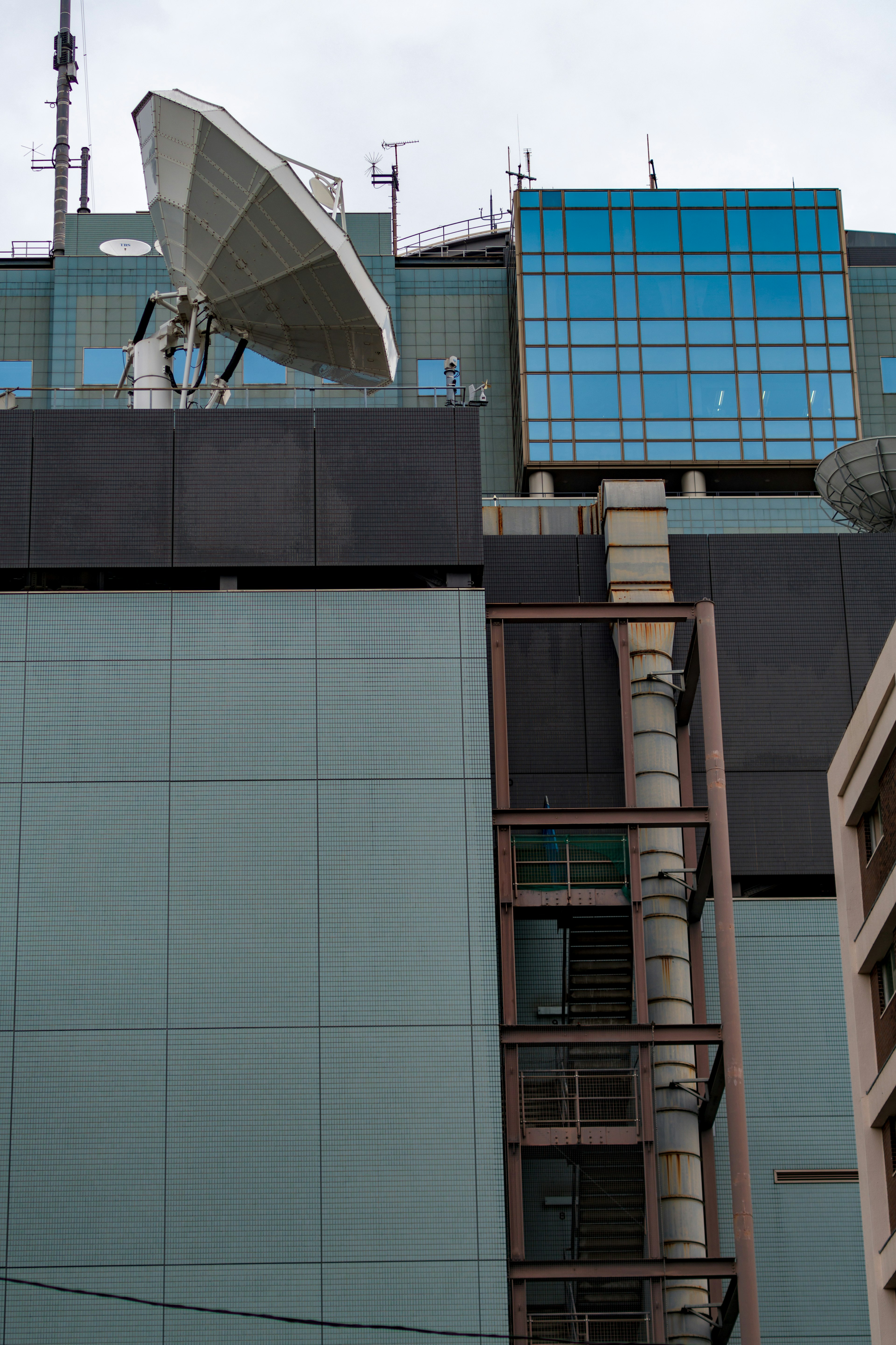 Large satellite antenna mounted on the side of a high-rise building with blue glass windows