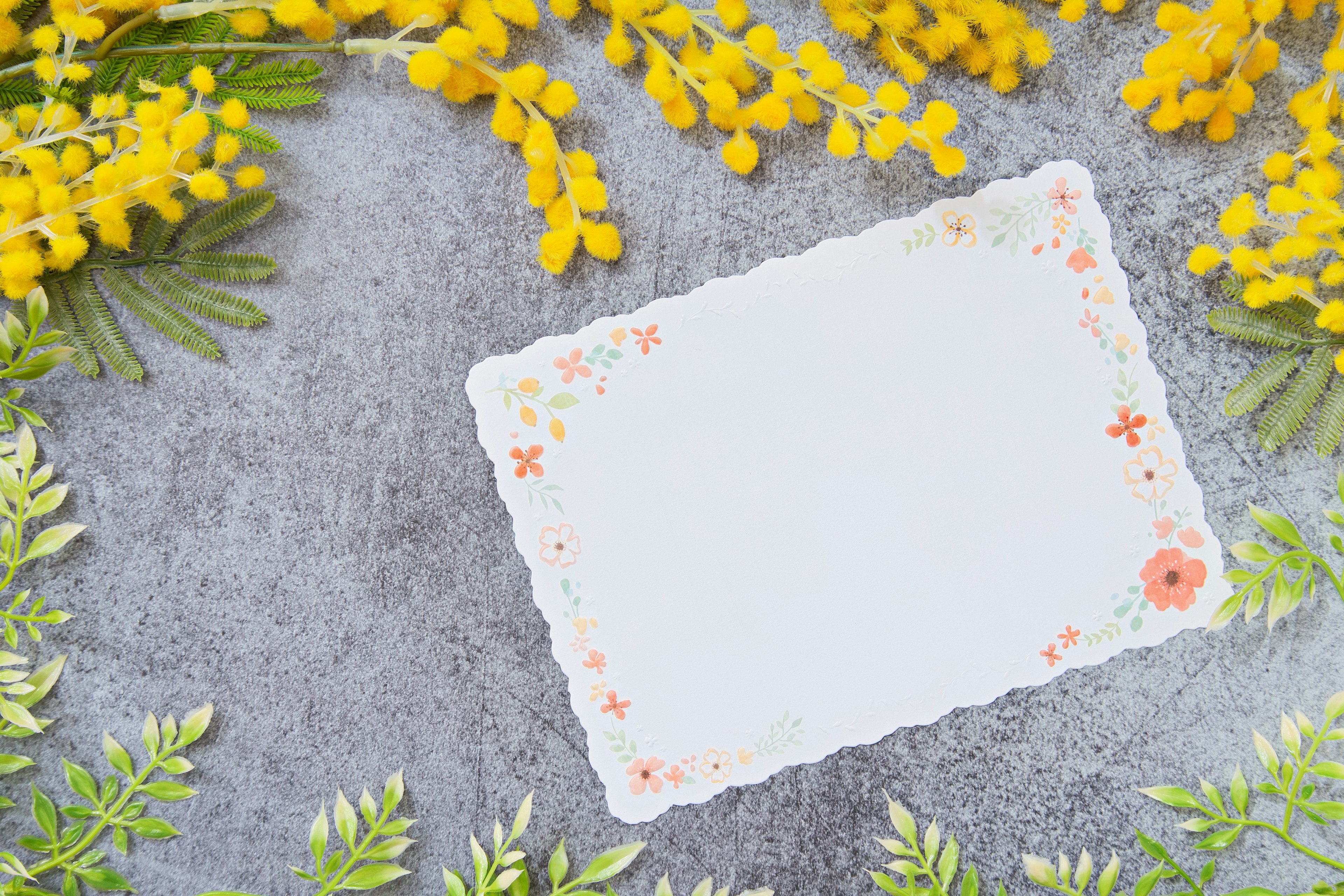 Ein weißes Notizblatt umgeben von gelben Blumen und grünen Blättern