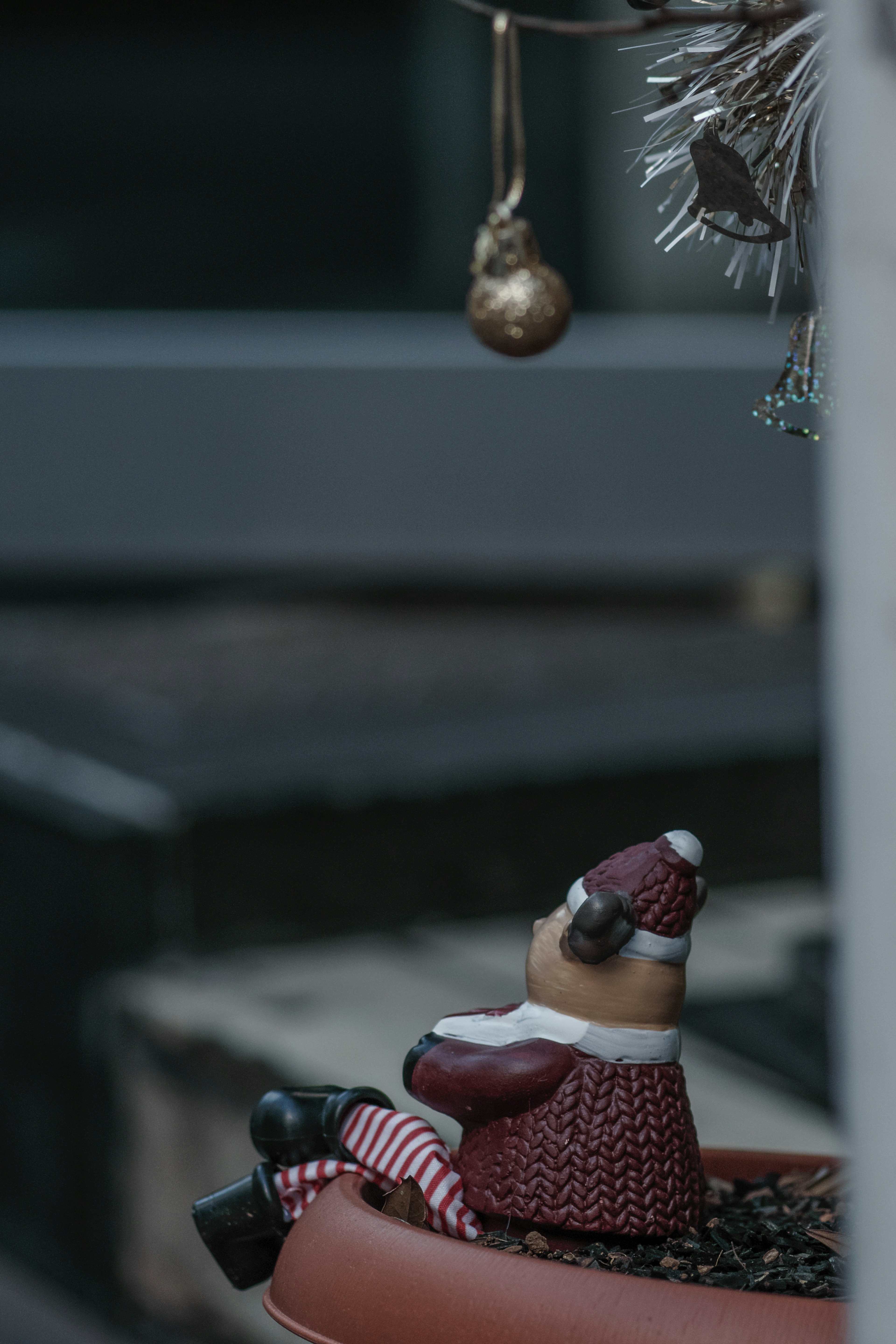 Ceramic Santa figurine sitting in a pot with a golden ornament hanging in the background