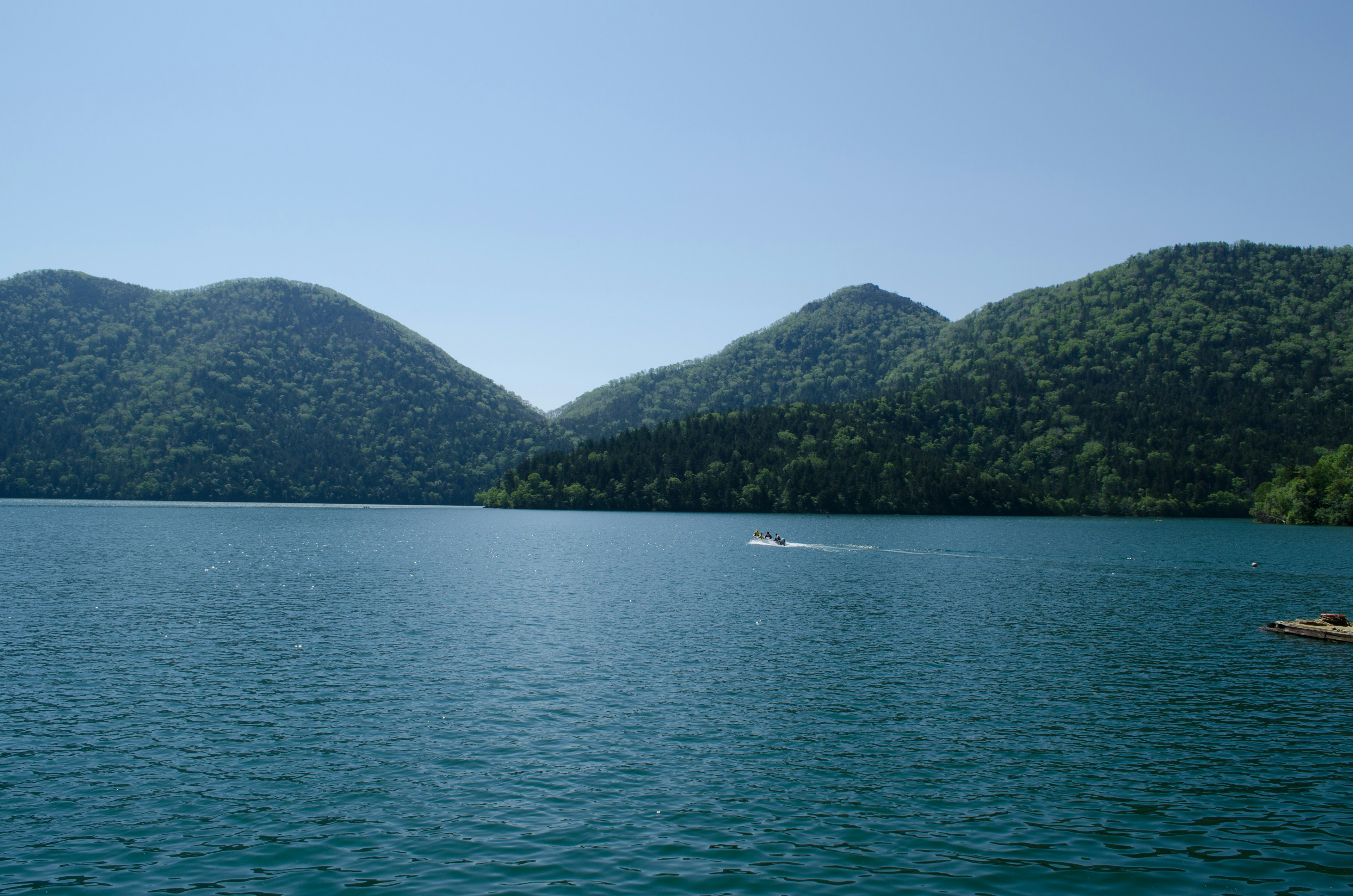 Landschaftsansicht eines Sees umgeben von grünen Bergen unter klarem blauen Himmel