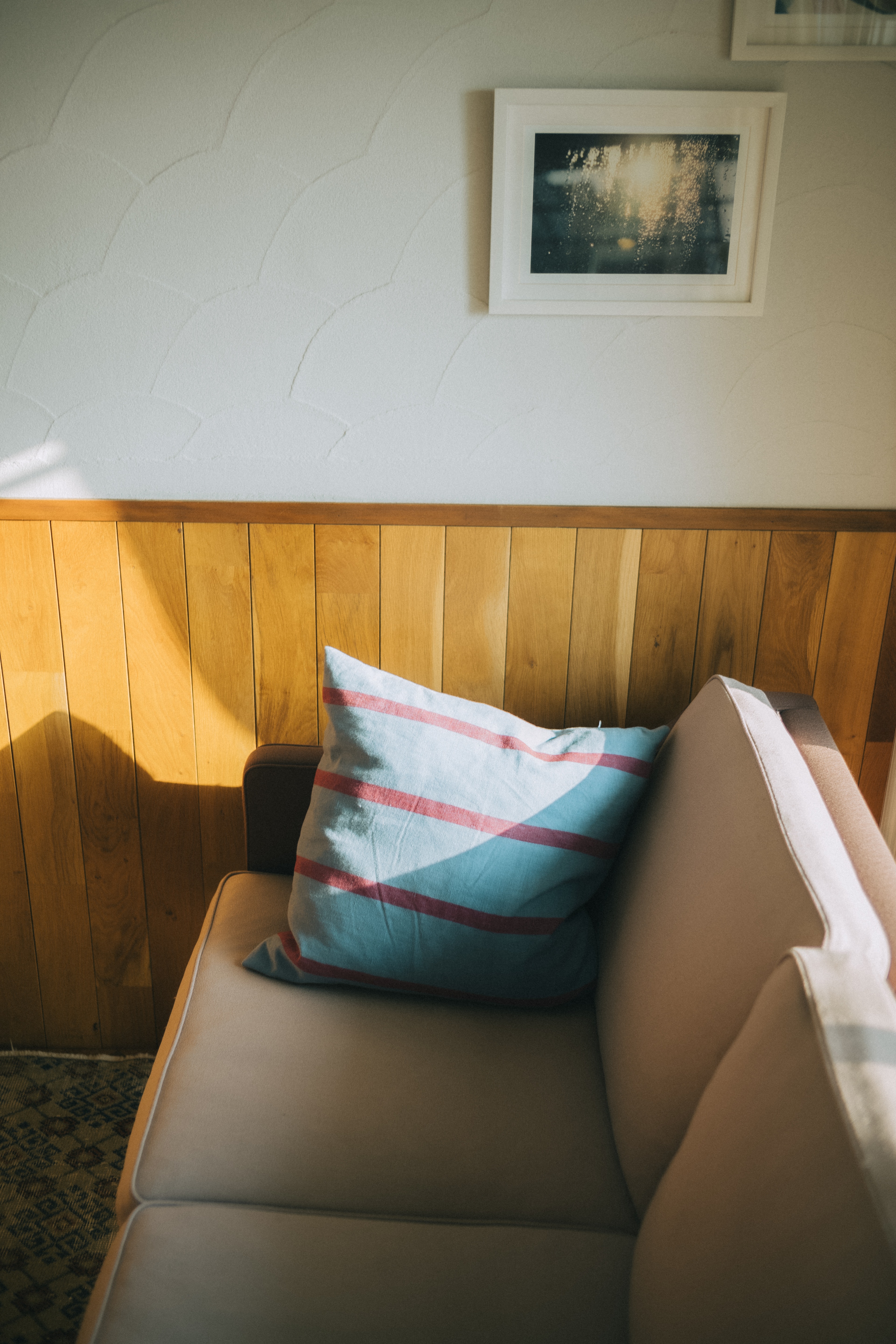 A section of a sofa with a colorful cushion and a wooden wall