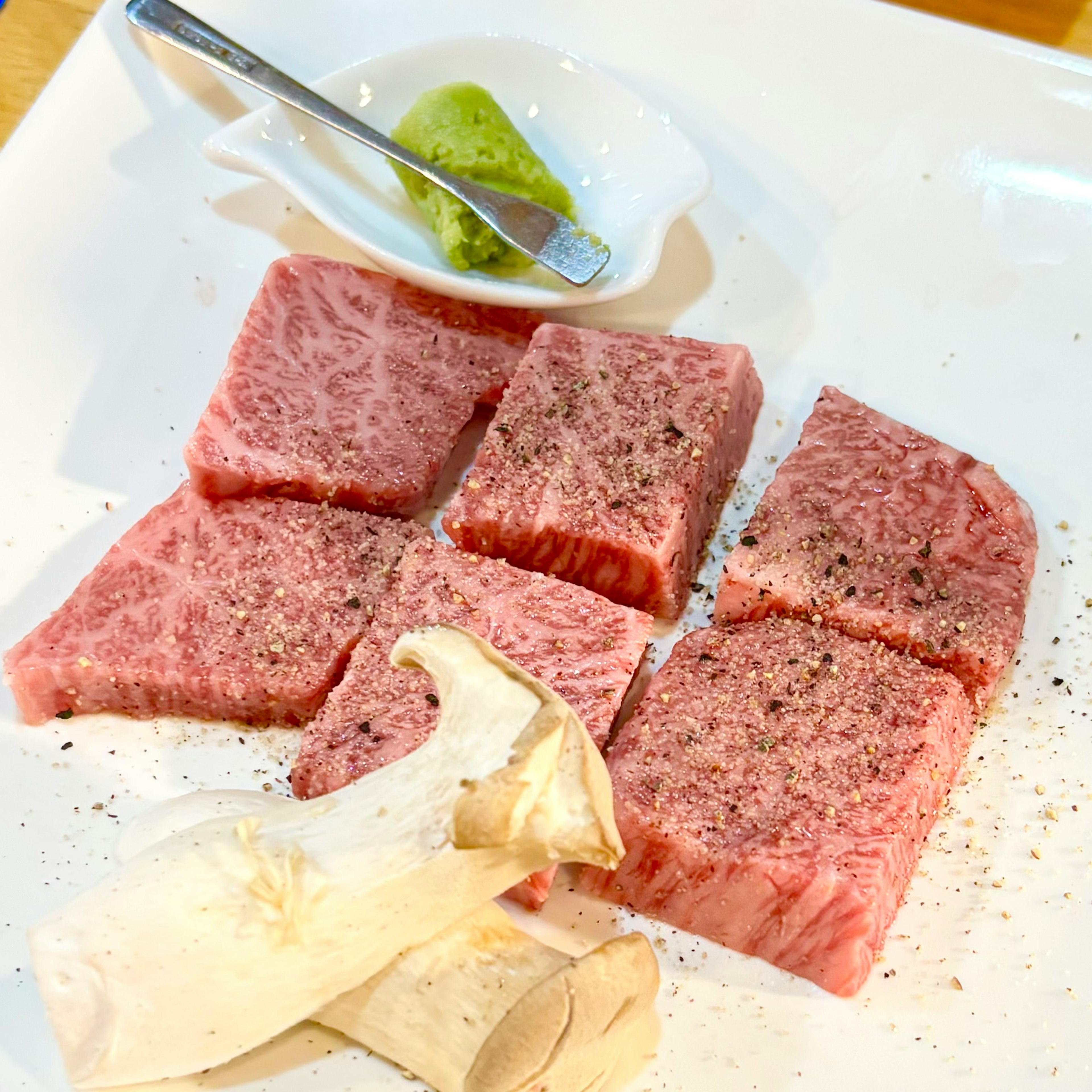 Kubus daging Wagyu segar disajikan di atas piring dengan wasabi dan jamur