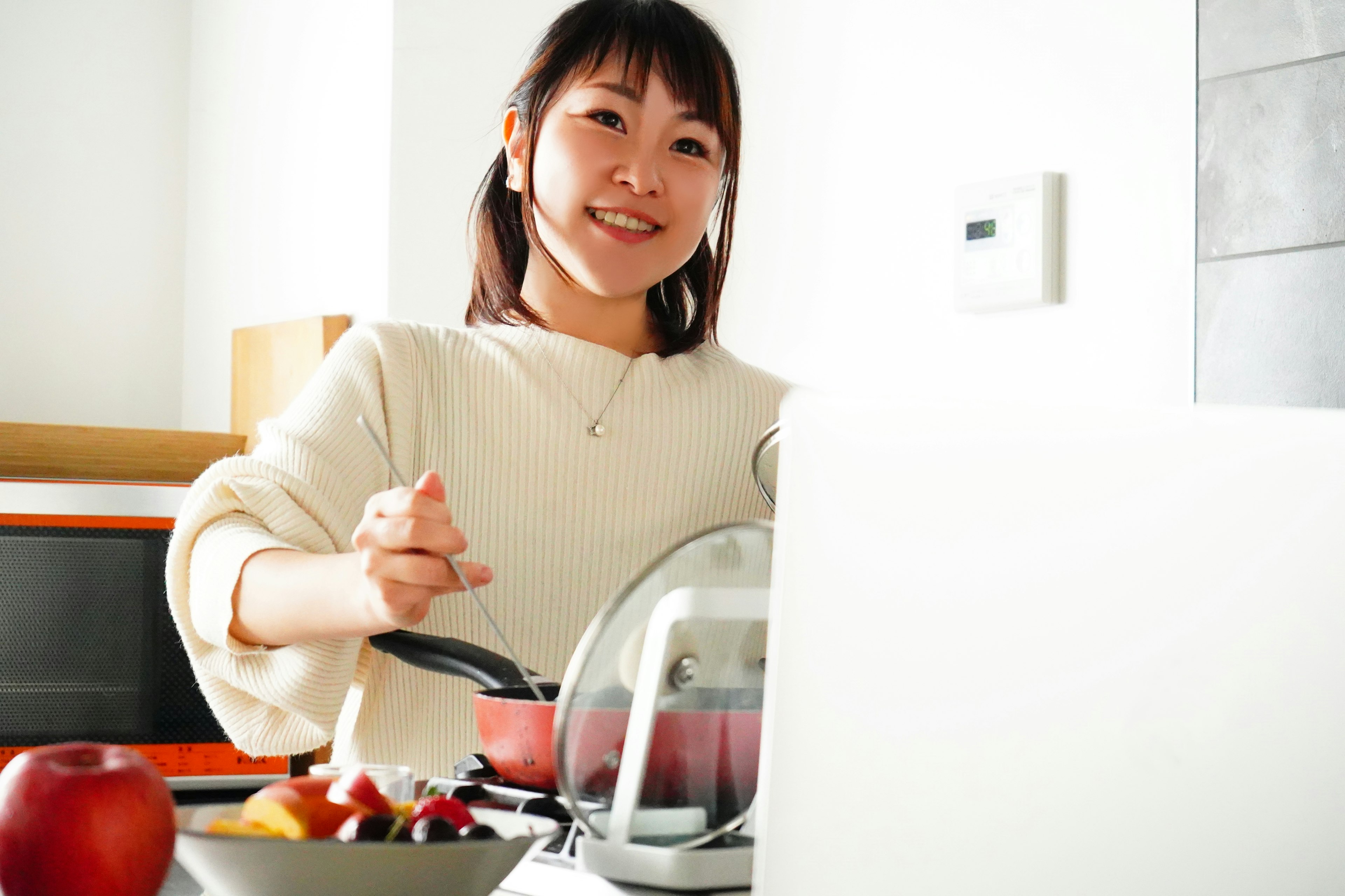 Wanita memasak di dapur tersenyum sambil mengaduk panci