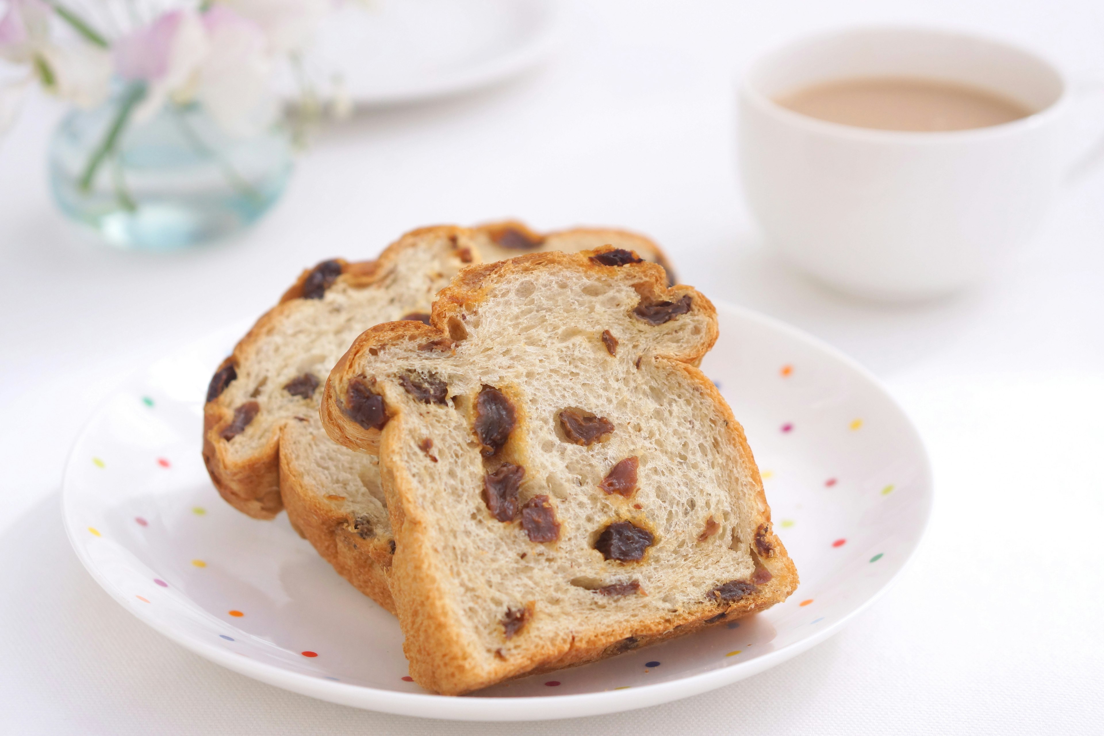 スライスされたレーズンパンが白いプレートに盛り付けられコーヒーが背景にある