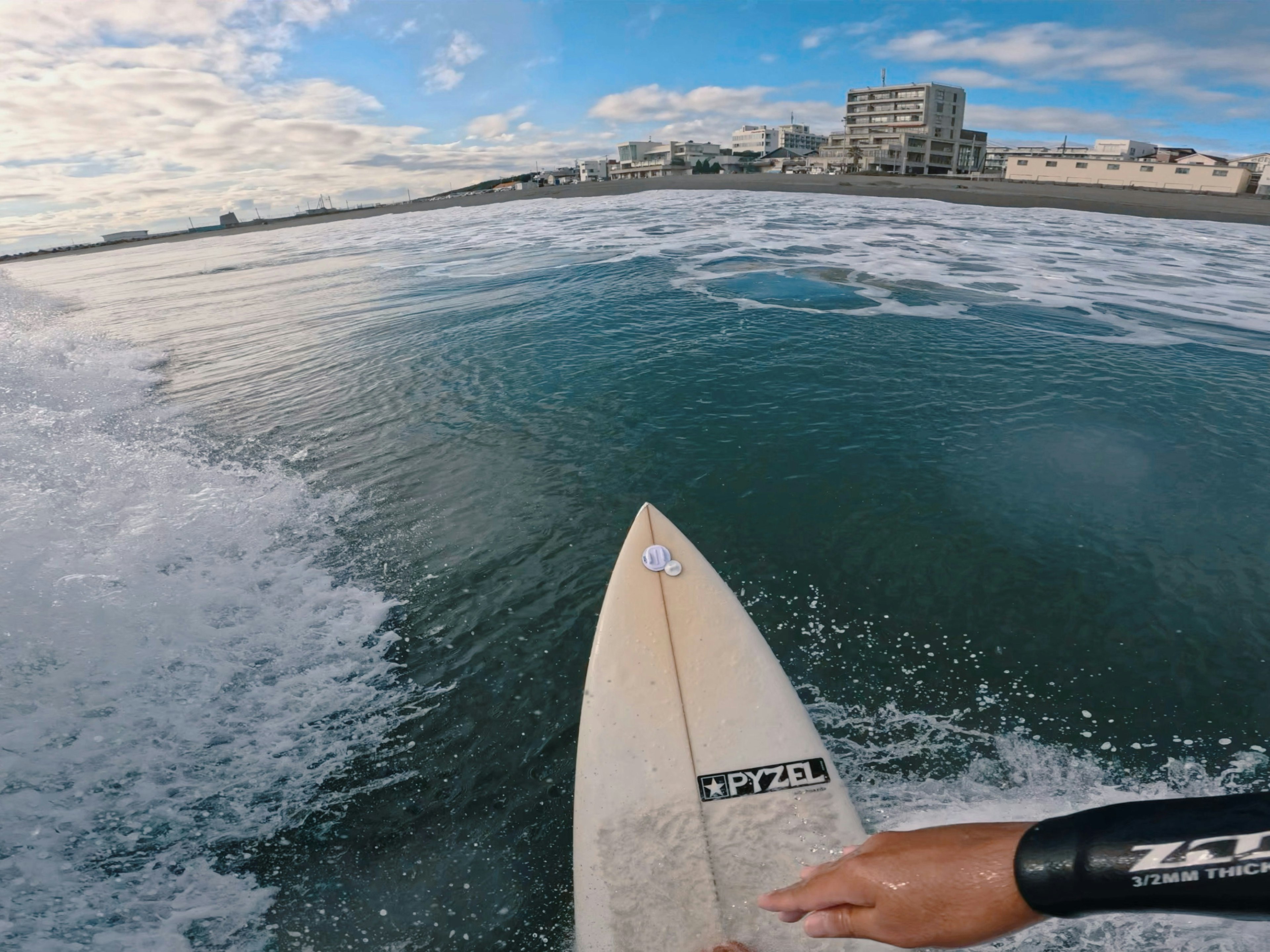 Hand on a surfboard with waves and a coastline in the background