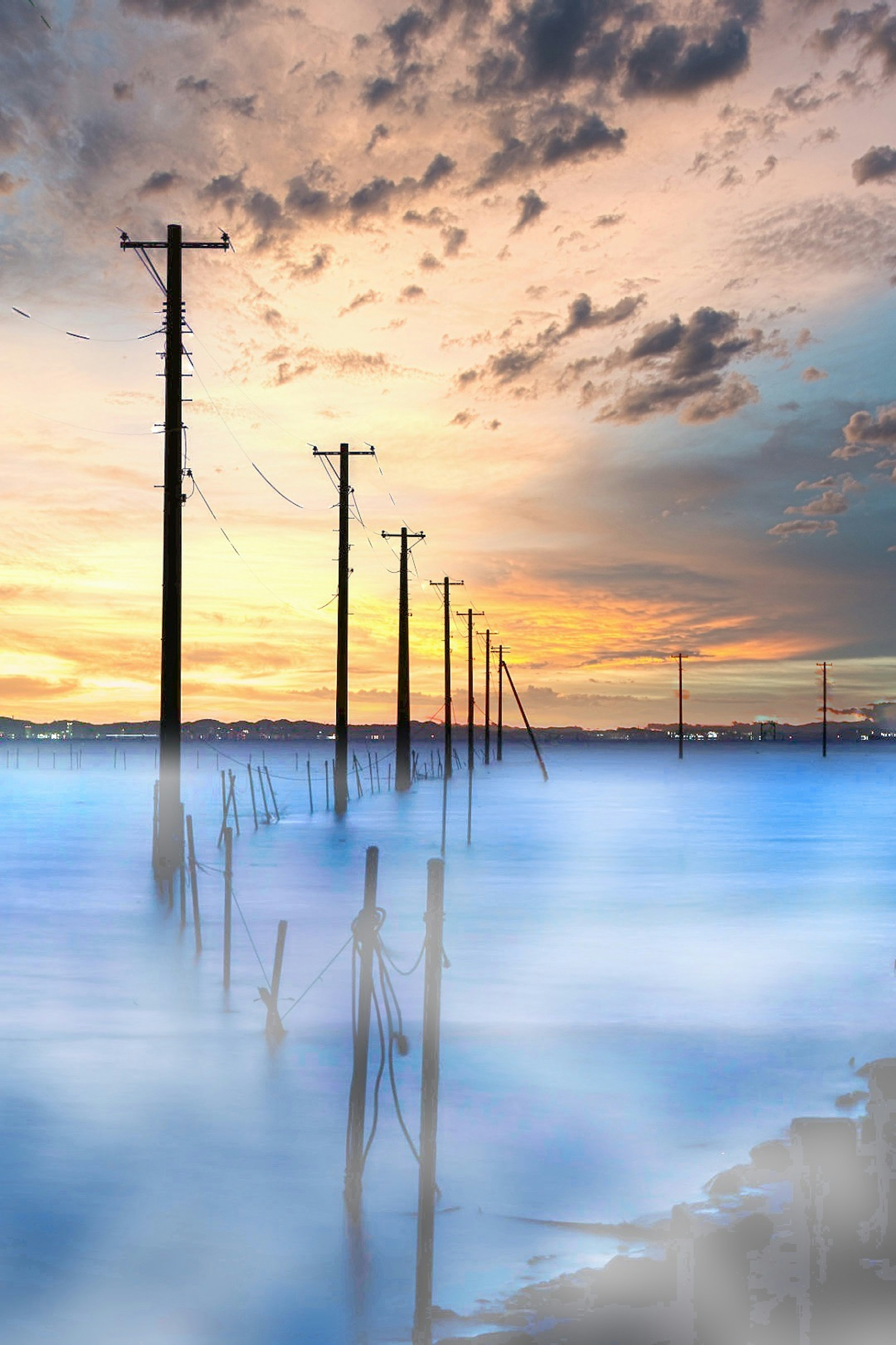 Une rangée de poteaux électriques enveloppés de brouillard contre un ciel de coucher de soleil magnifique