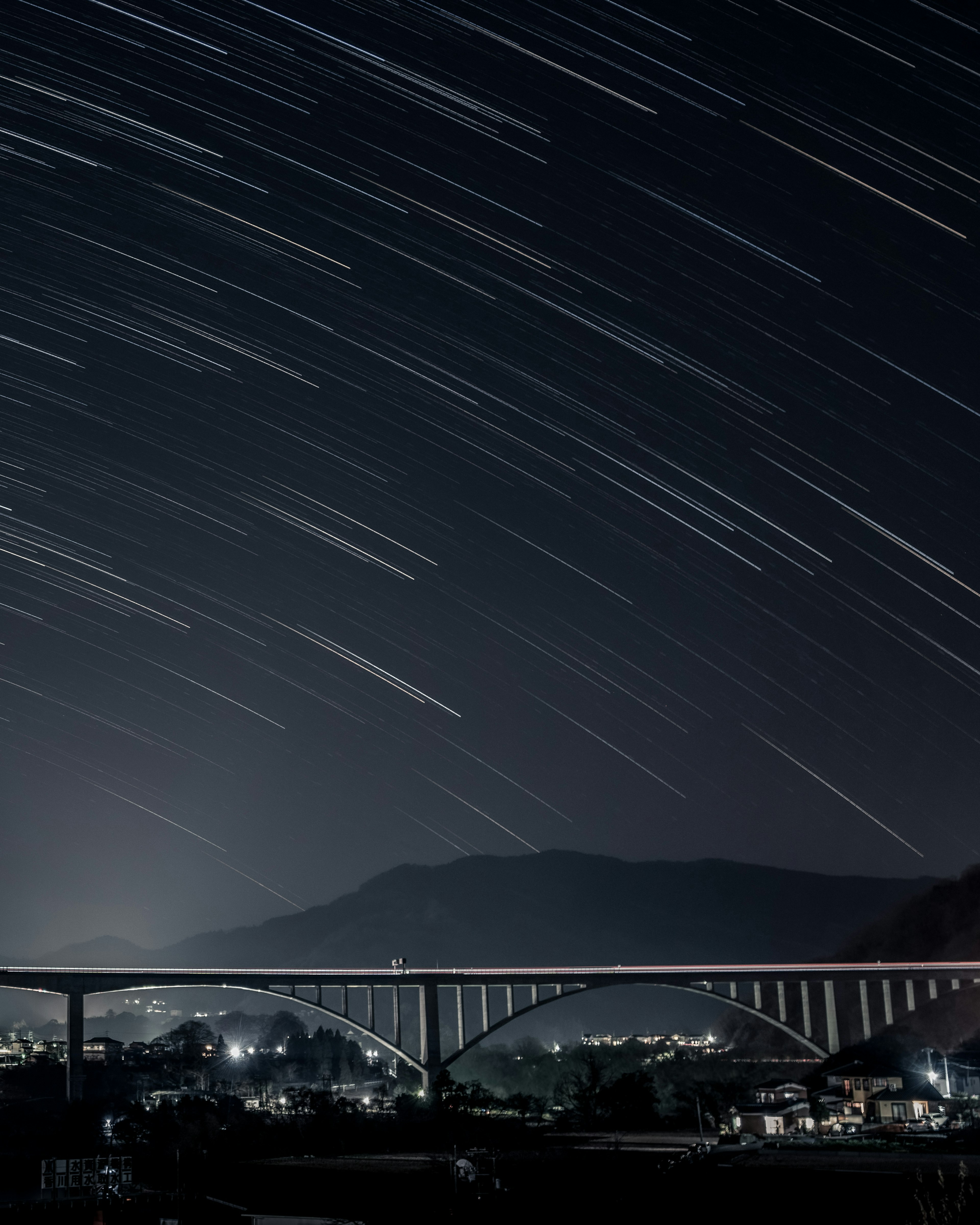 Cielo nocturno con estelas de estrellas y vista de un puente