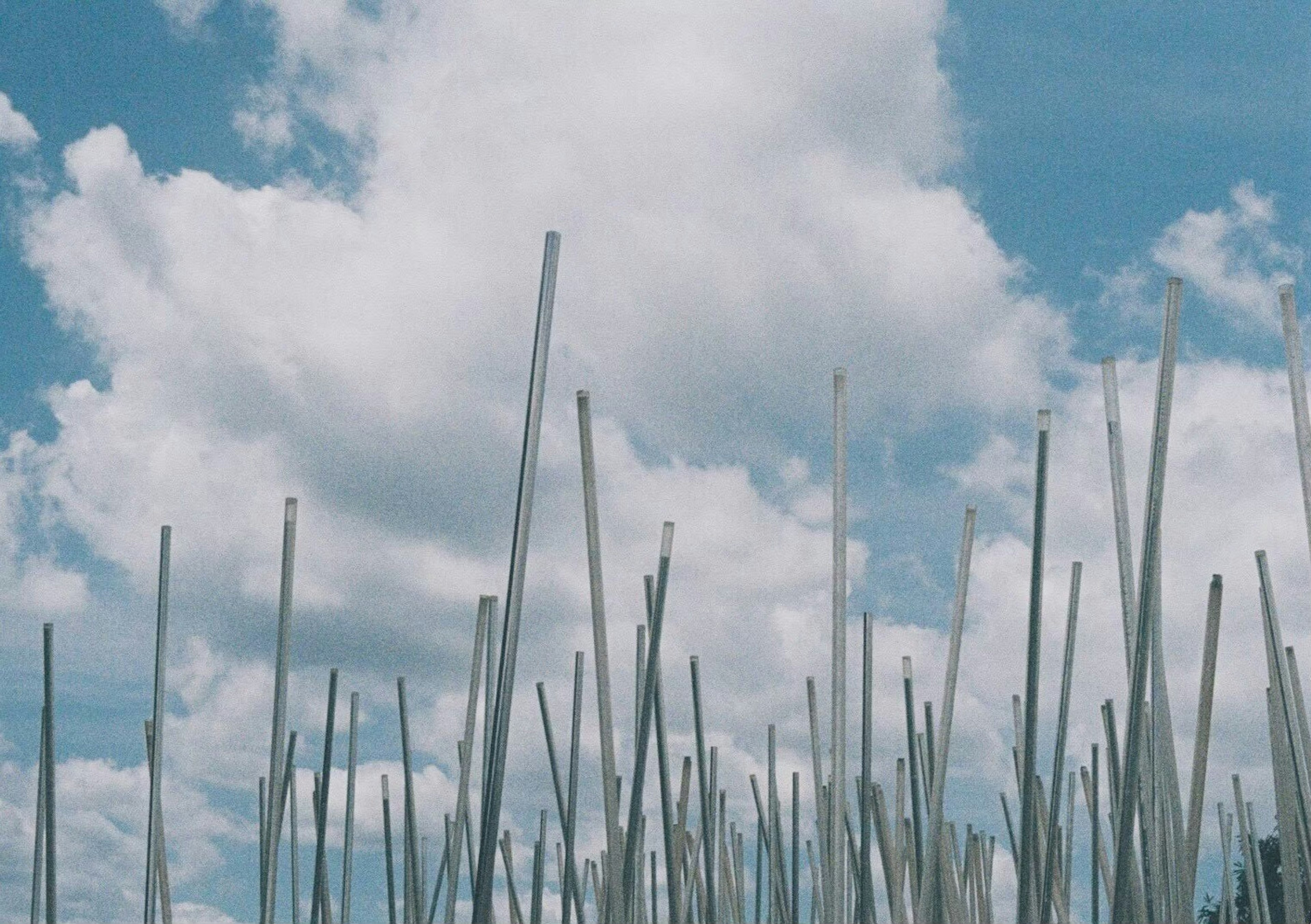 Un paisaje con varillas metálicas que se elevan bajo un cielo azul y nubes blancas